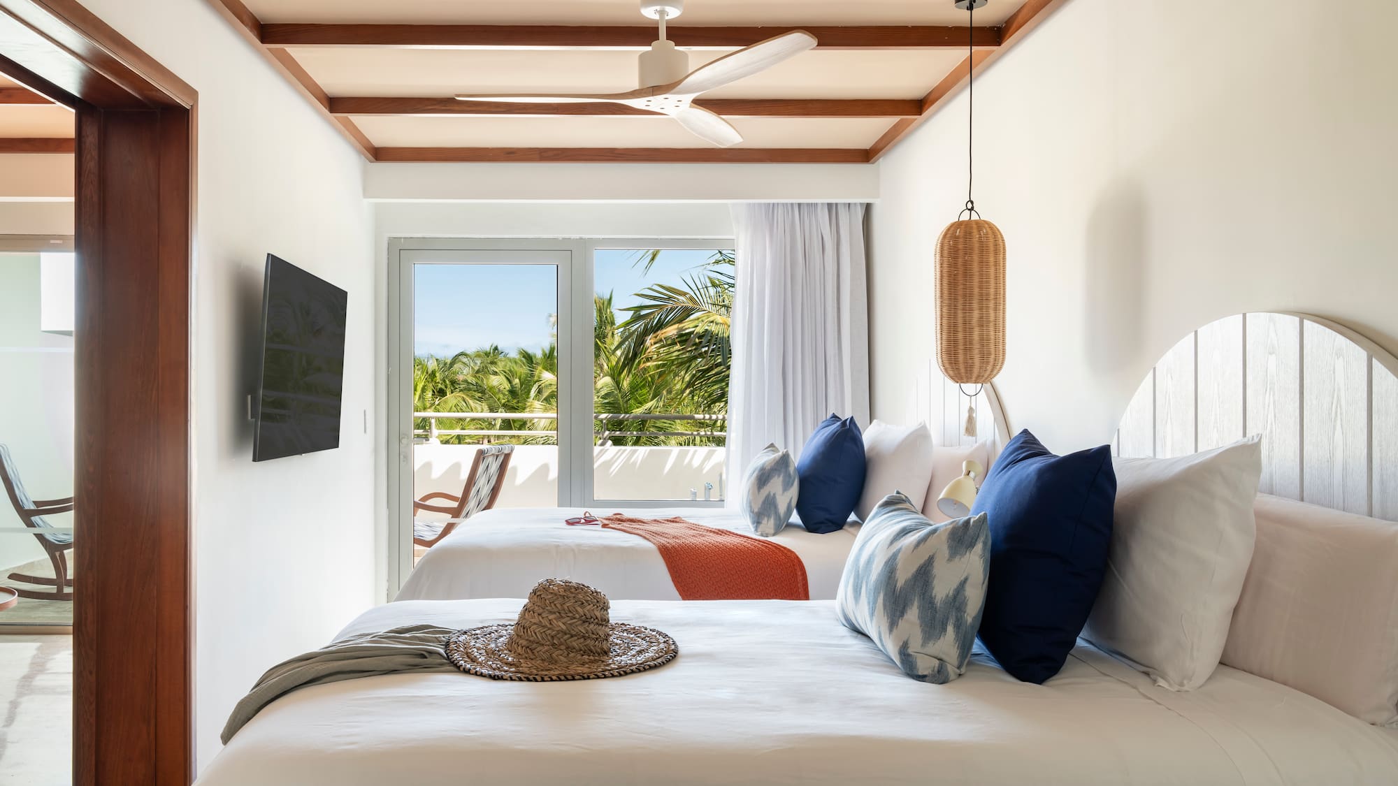 Tropical hotel room, two beds, balcony with palm tree view, ceiling fan.