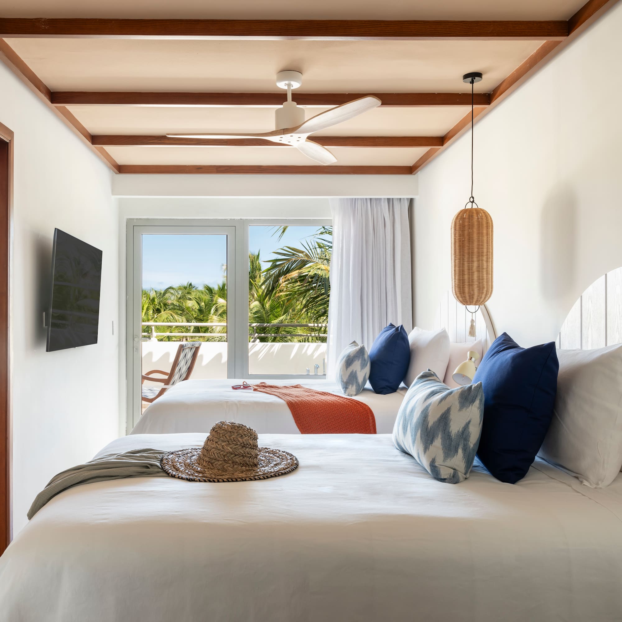 Tropical hotel room, two beds, balcony with palm tree view, ceiling fan.