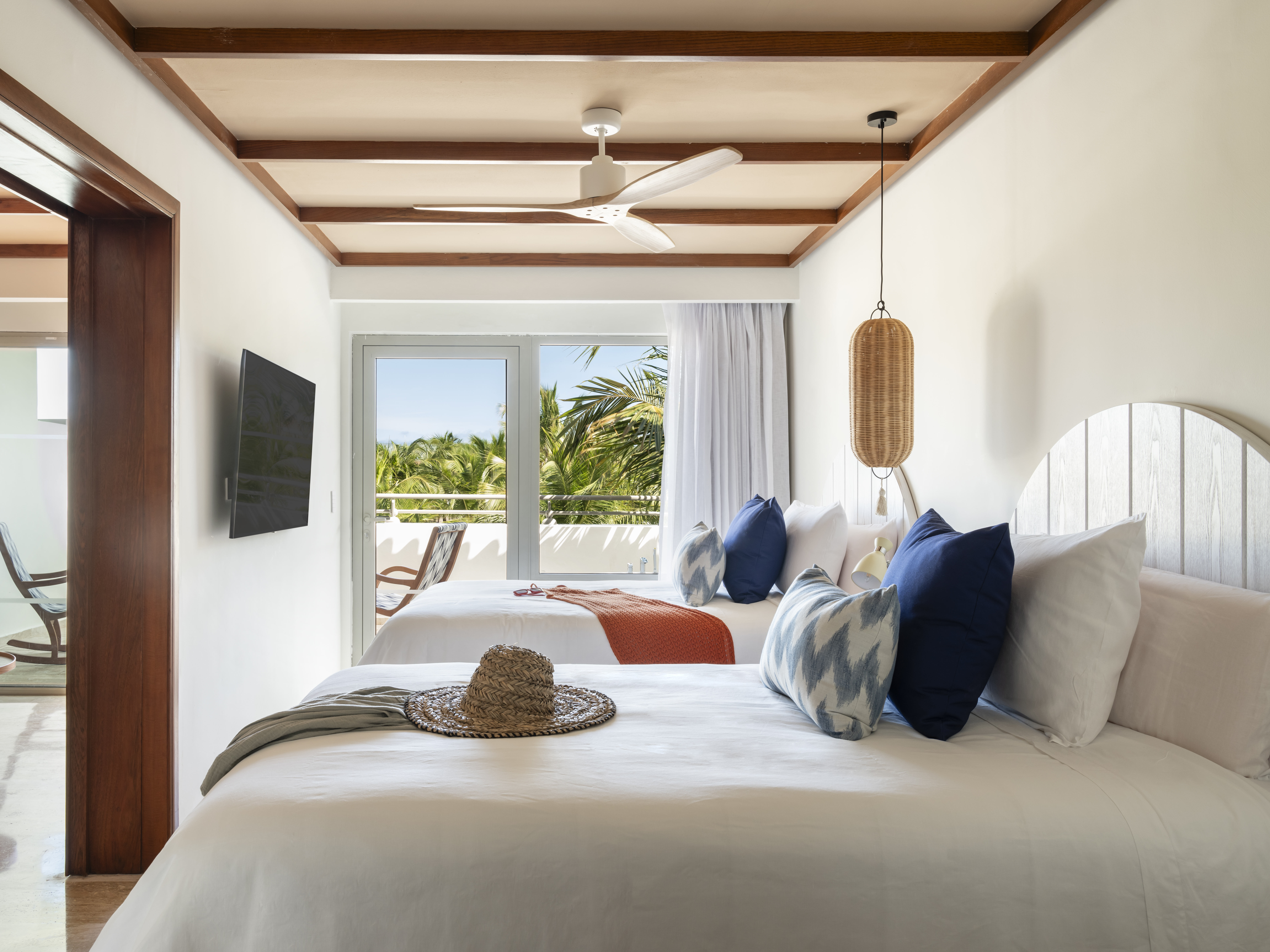 Tropical hotel room with two beds, balcony, palm trees, and ceiling fan.