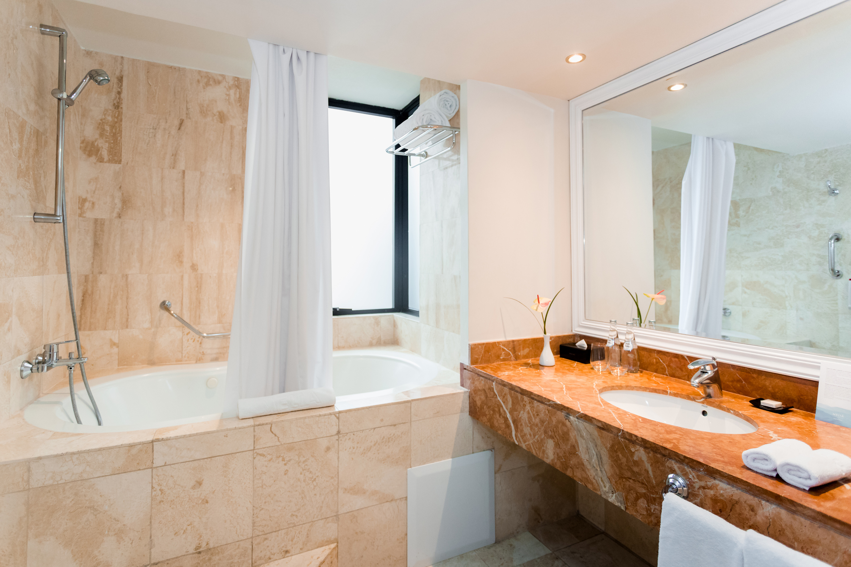 Modern hotel bathroom with beige tiled tub/shower and marble vanity.