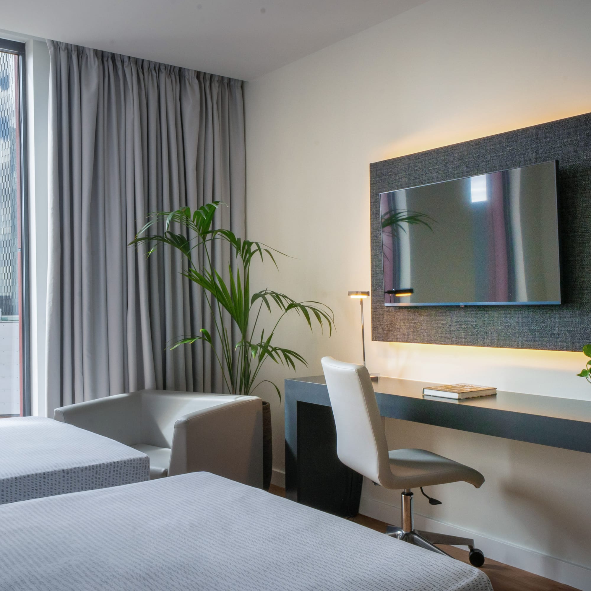 Modern hotel room with twin beds, city view, desk, and wall-mounted TV.