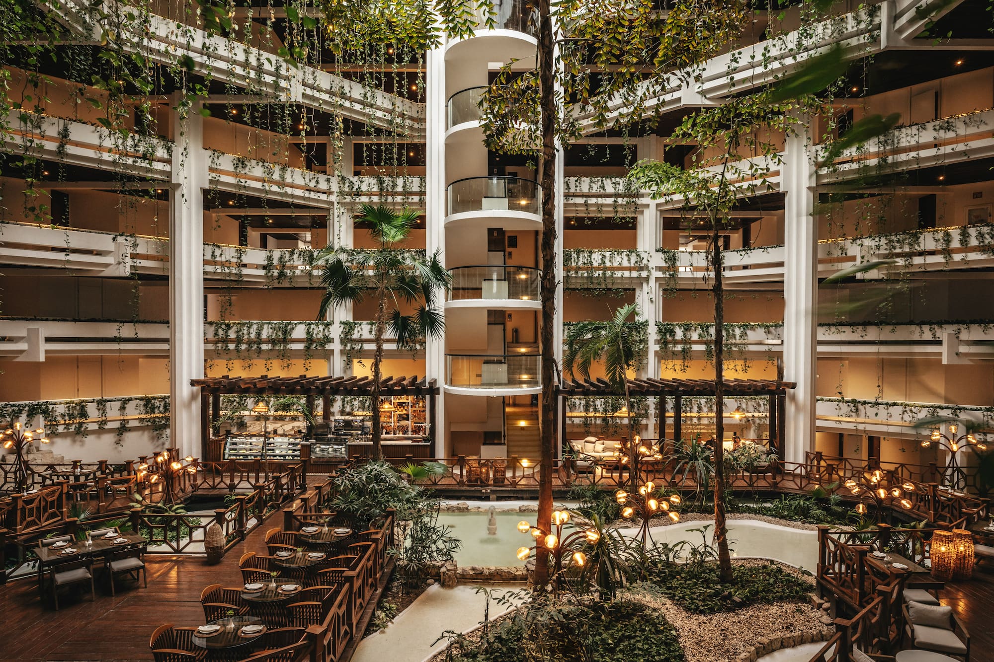 Lush hotel atrium with spiral elevator, indoor garden, and elegant dining.