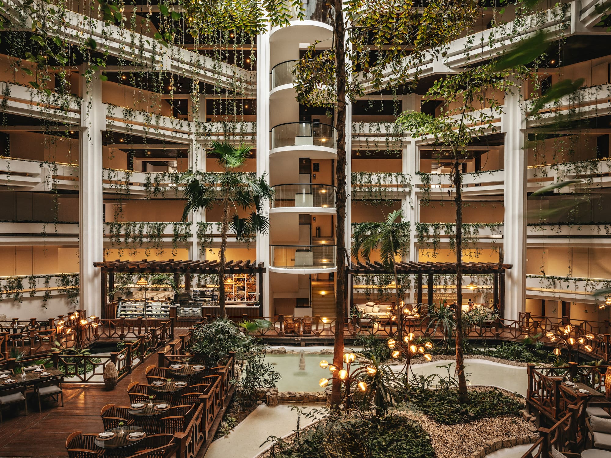 Lush hotel atrium with spiral elevator, indoor garden, and elegant dining.