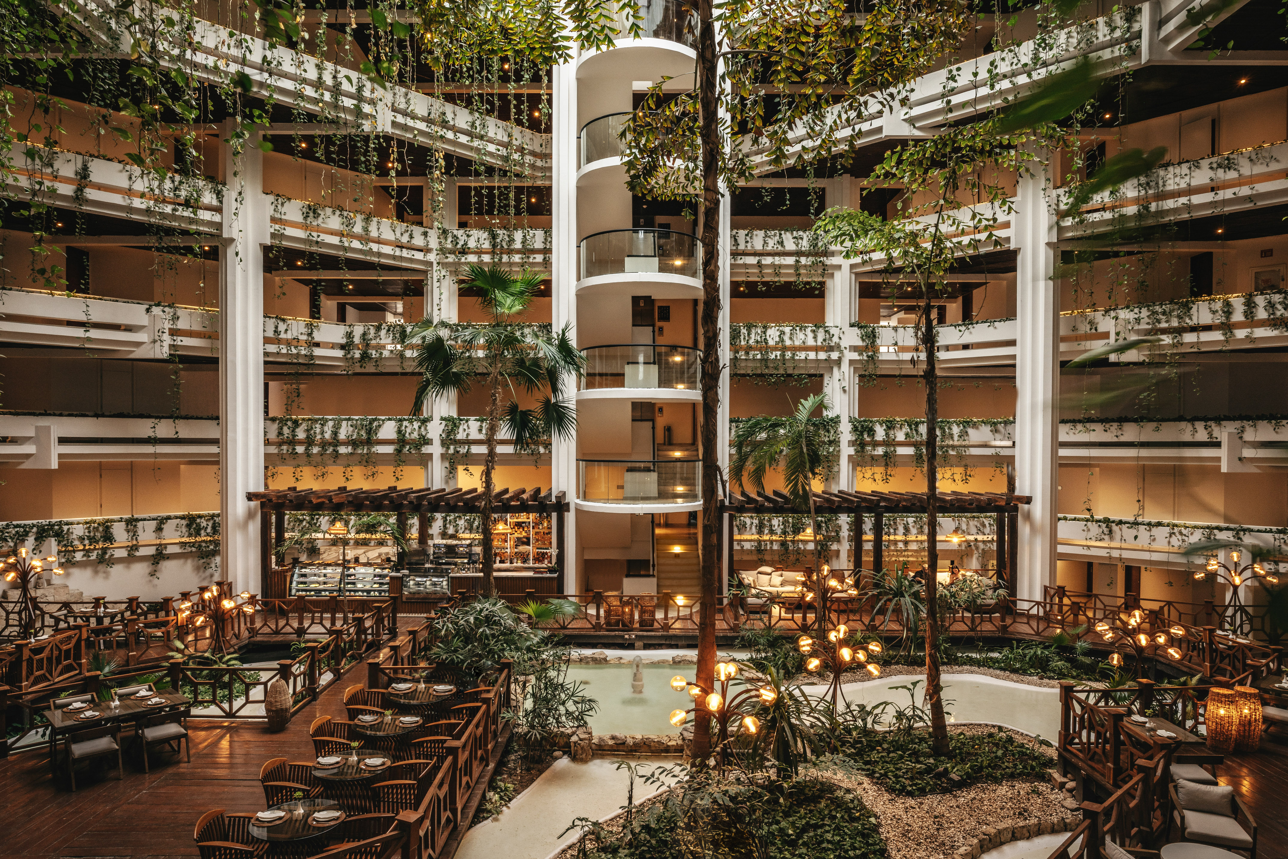Lush hotel atrium with spiral elevator, indoor garden, and elegant dining.