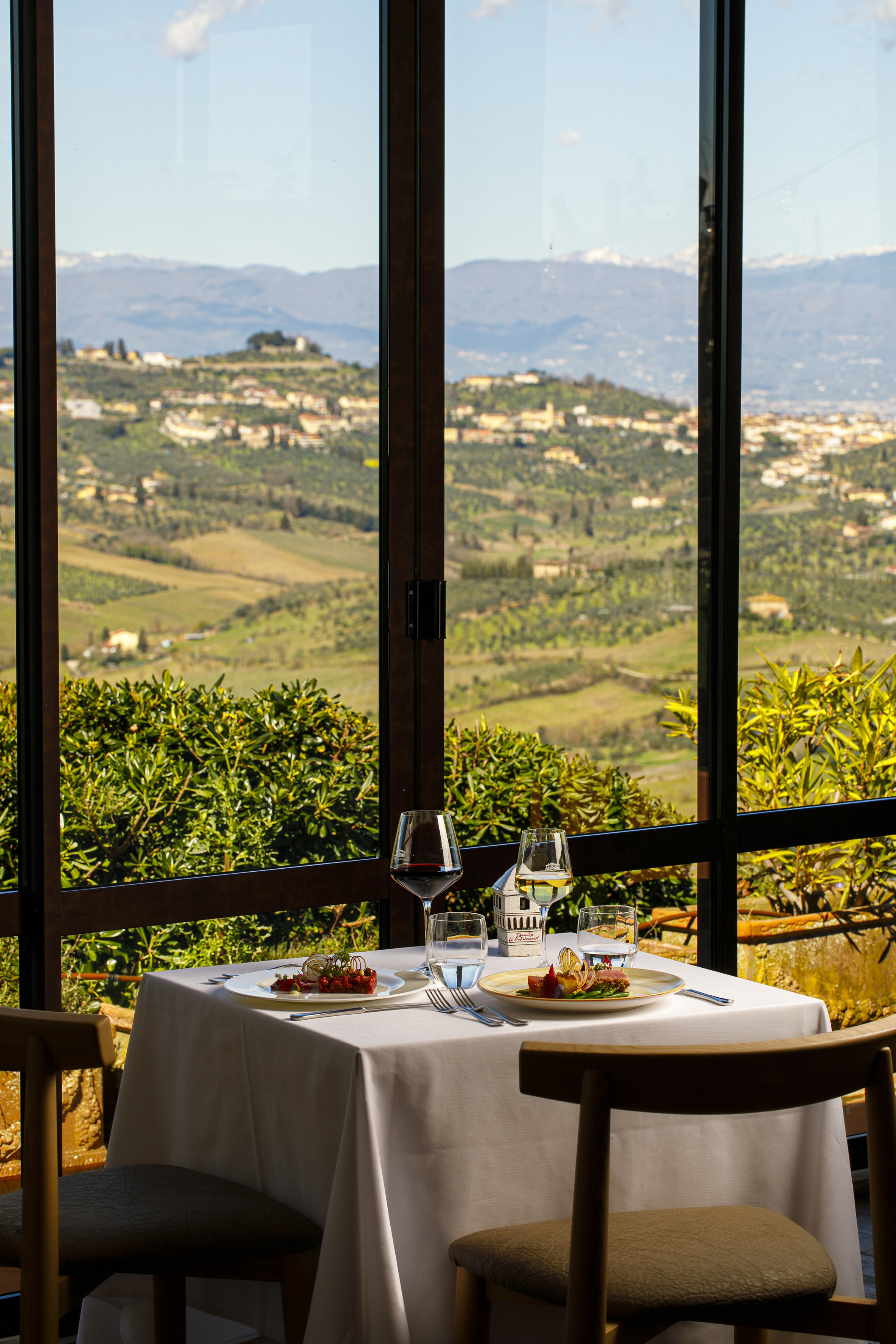 Fine dining table with wine, gourmet food, and panoramic Tuscany hill view.