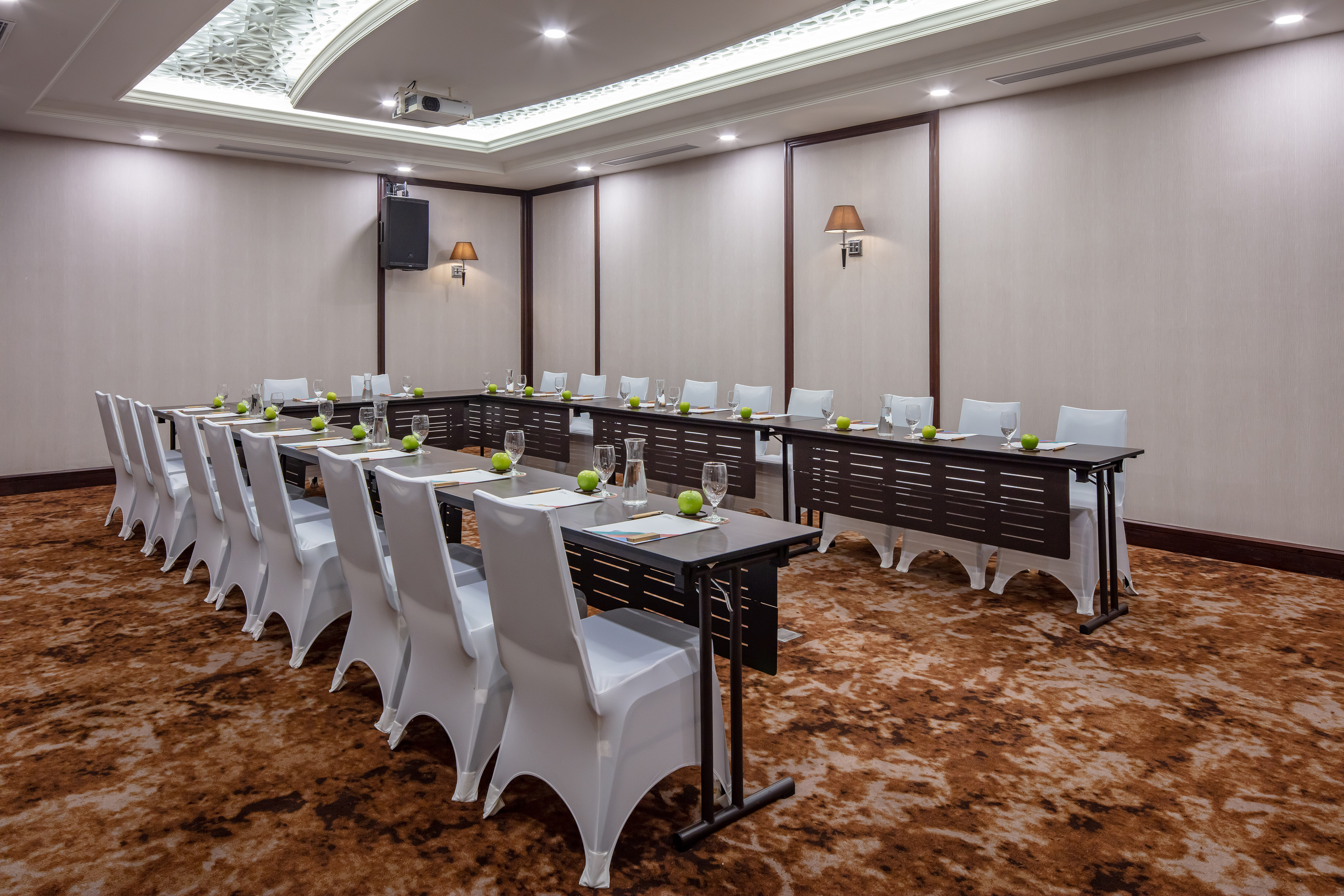 U-shaped conference room with white chairs, tables, projector, and green apples.
