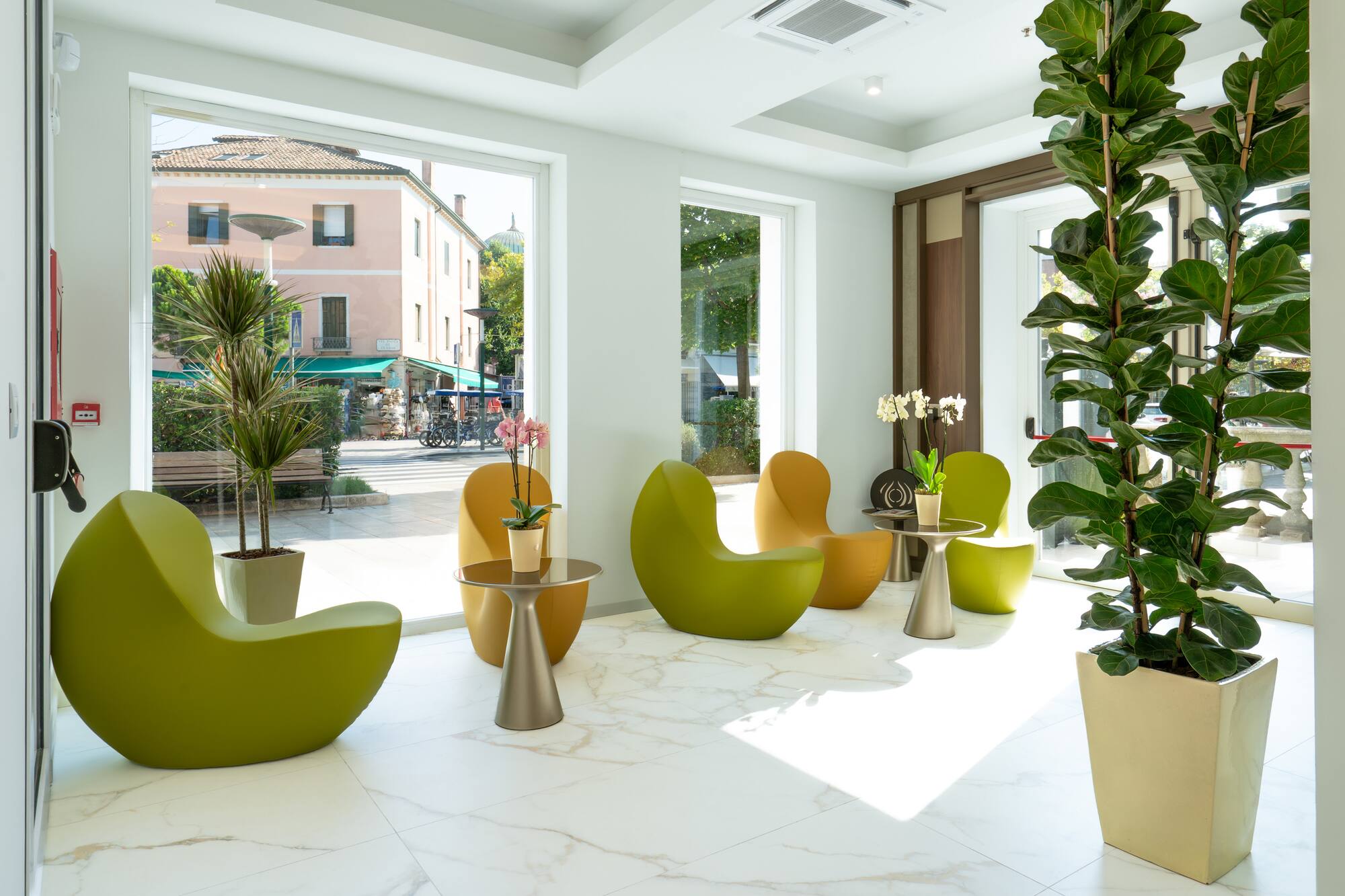 Modern lounge with green & yellow chairs, marble floor, large windows, and plants.