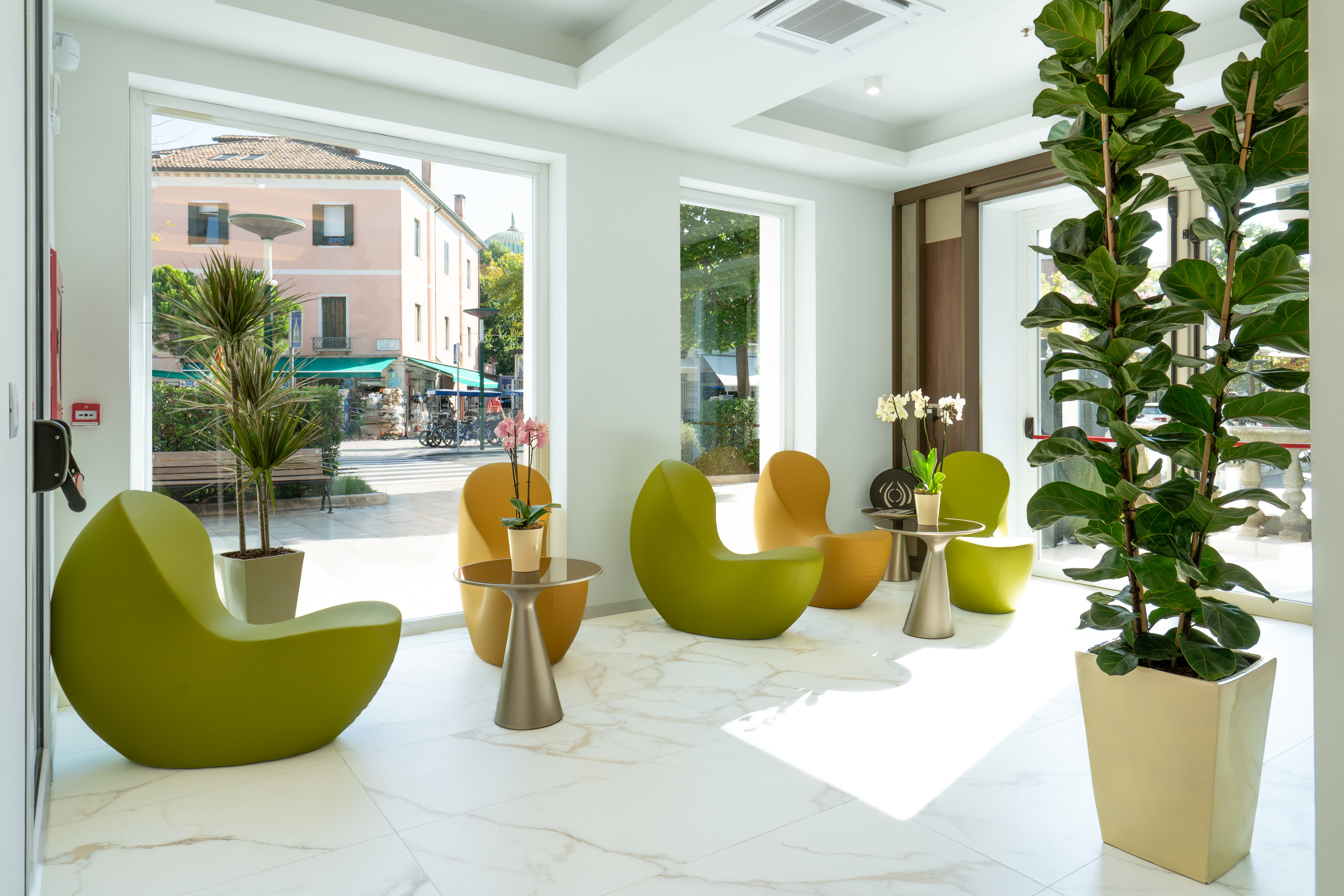 Modern lounge with green & yellow chairs, marble floor, large windows, and plants.