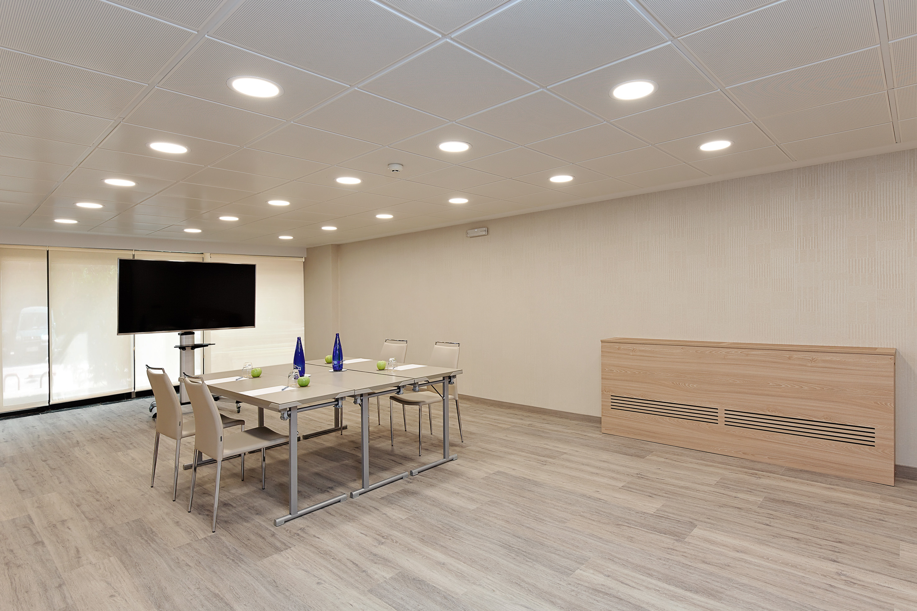 Modern conference room with screen, long table, chairs, and neutral interior.