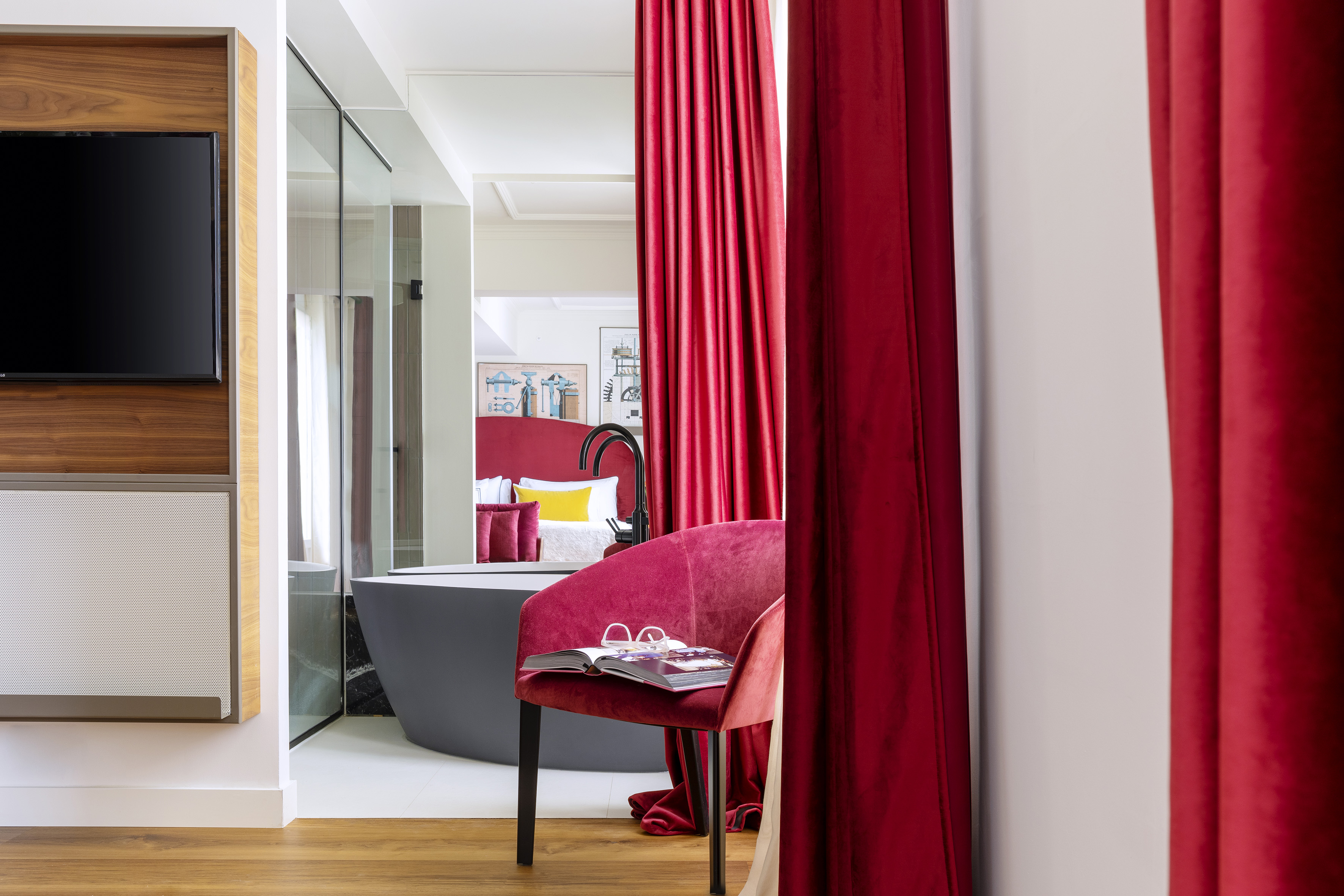 Modern hotel suite with red velvet chair, curtains, and freestanding bathtub.