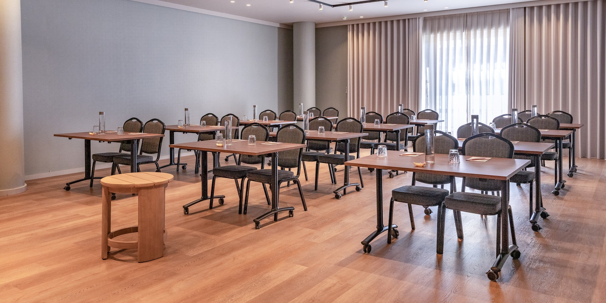 Modern conference room with tables, chairs, water, and light wood floor.