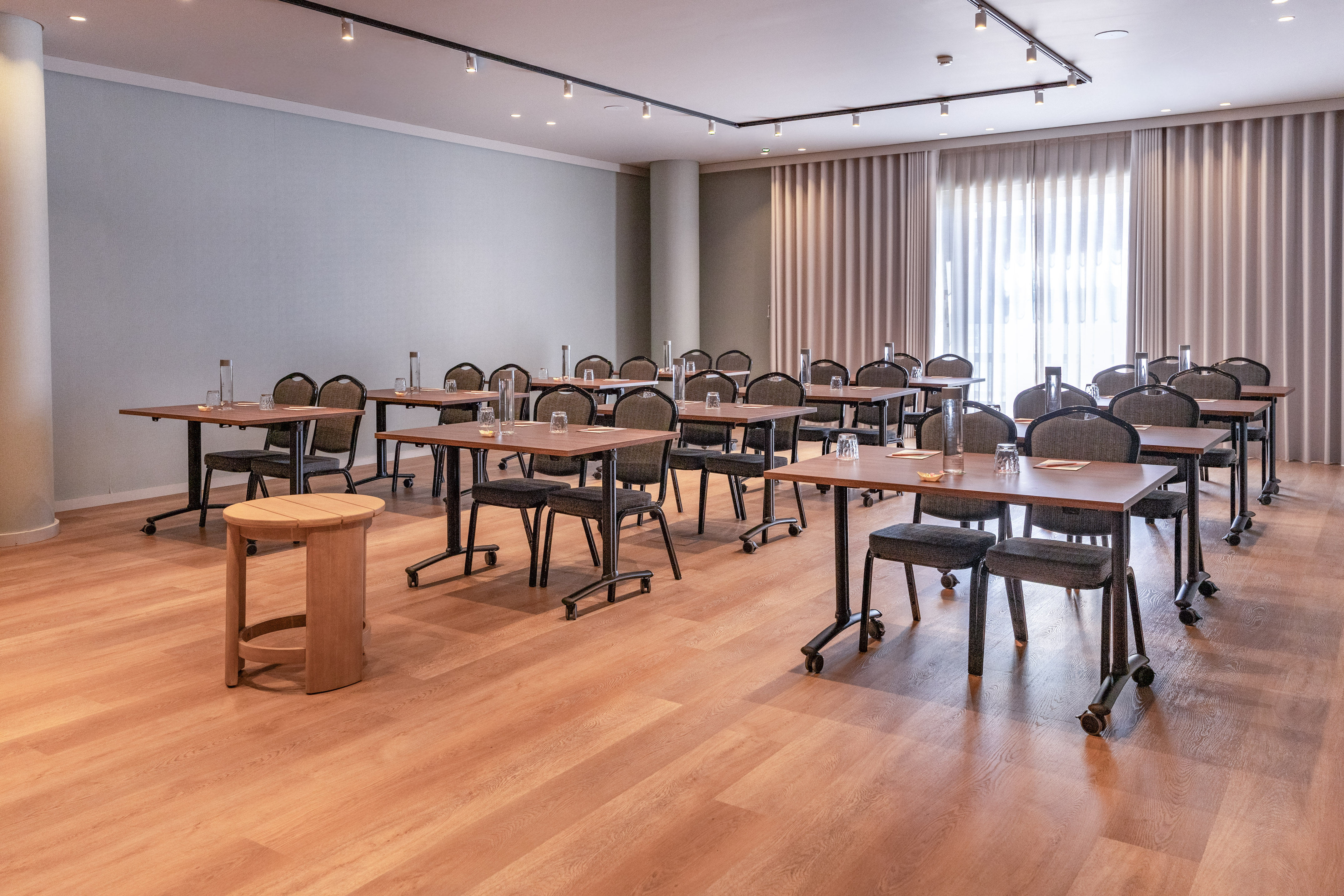 Modern conference room with tables, chairs, water, and light wood floor.