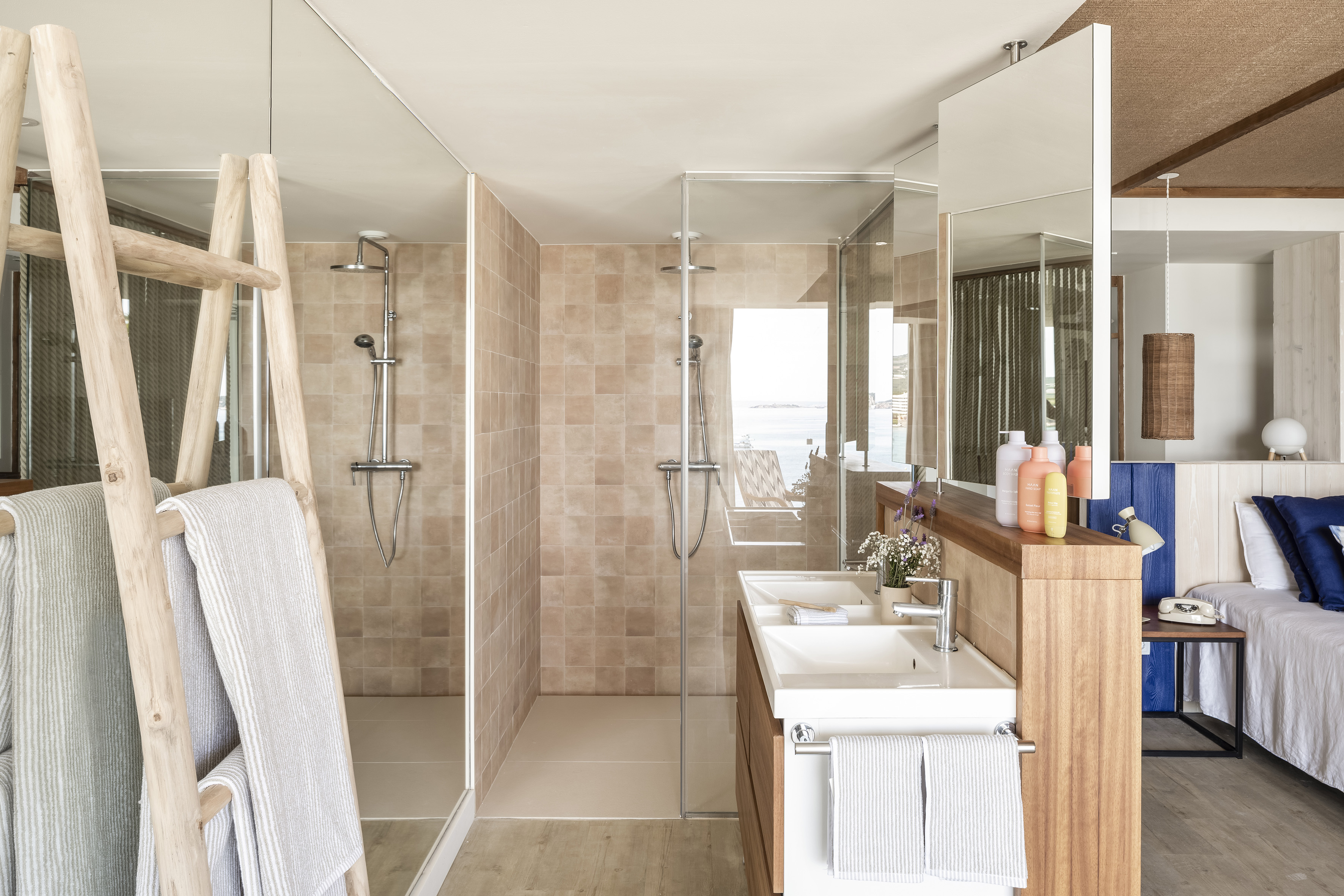 Modern bathroom: walk-in shower, dual sinks, wood towel ladder, ocean view.