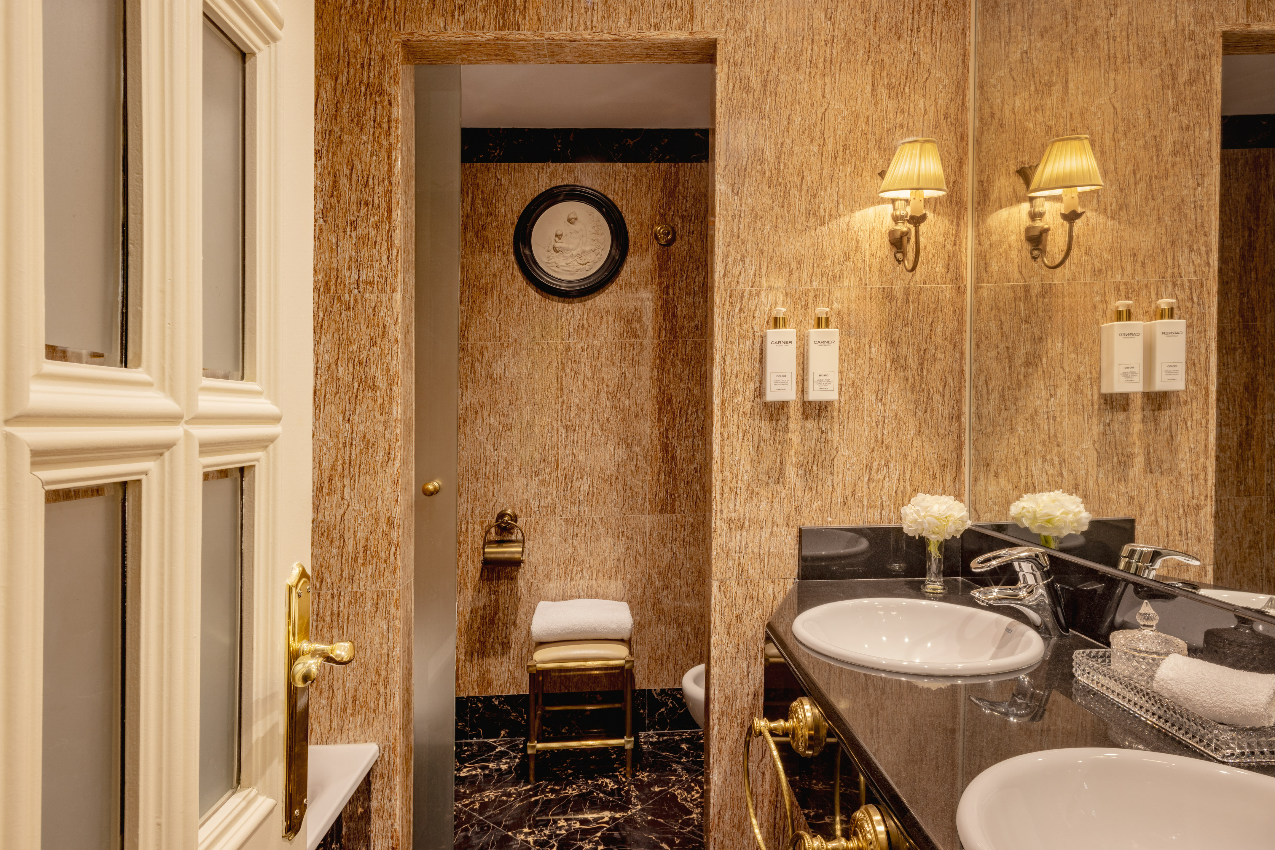 Luxury bathroom with black marble double vanity, gold fixtures, and textured walls.
