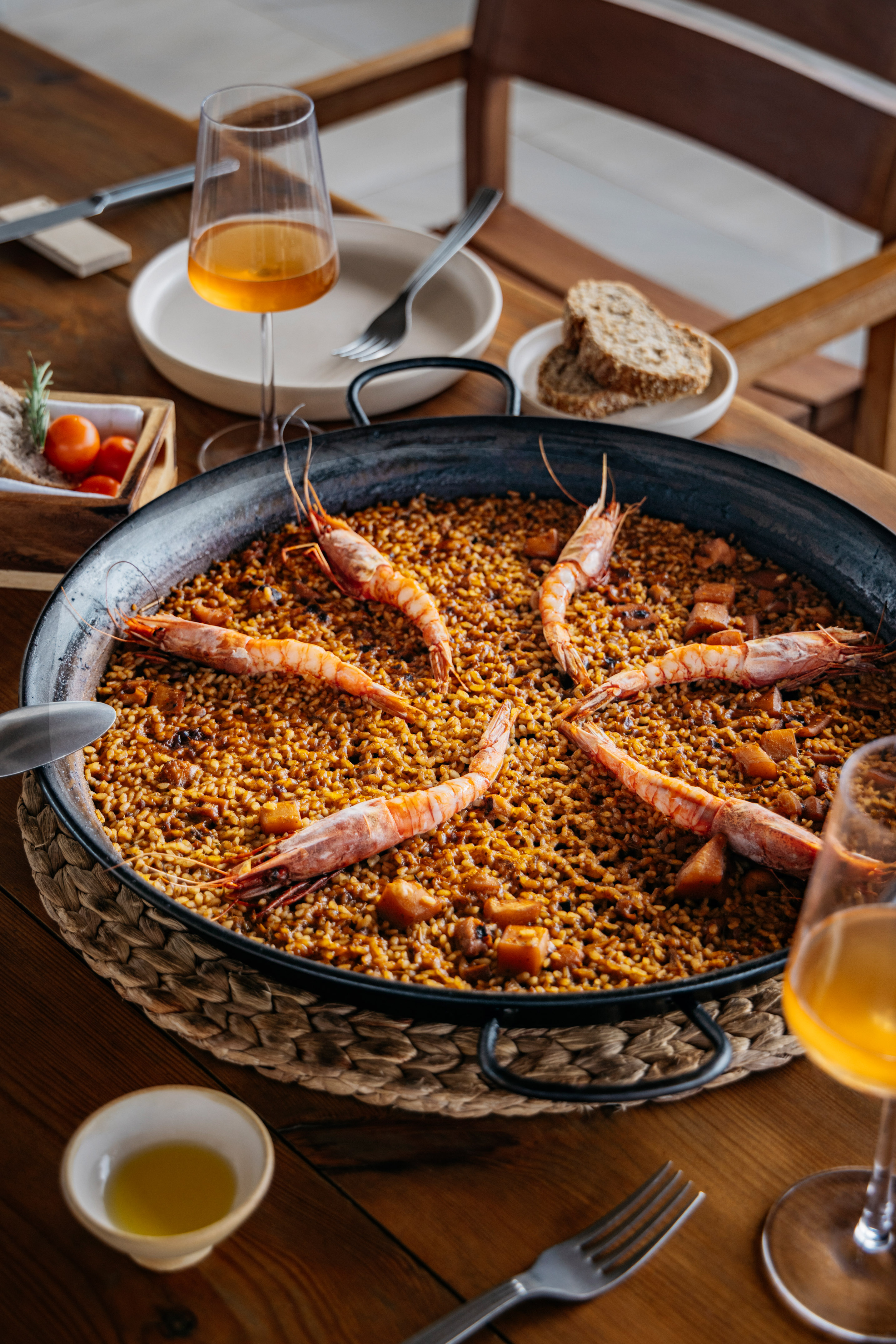 Spanish shrimp paella in a large pan on a wooden table with wine.