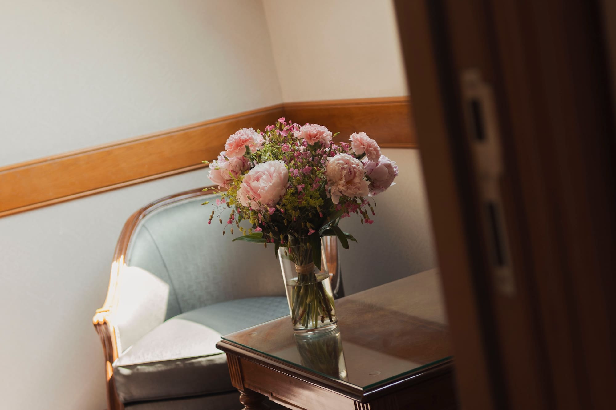Ramo de peonías rosas en mesa con sillón y luz natural de tragaluz.