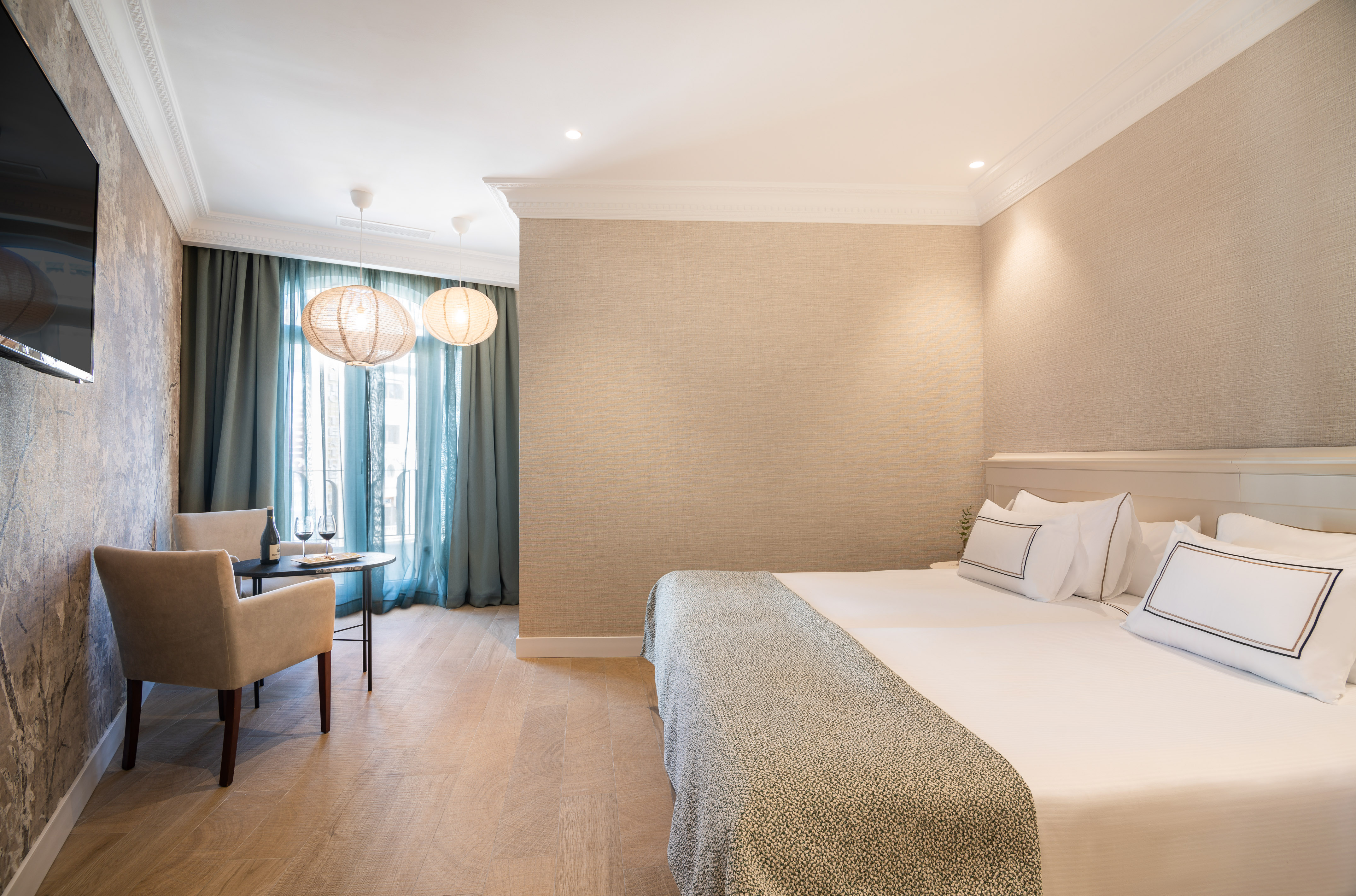 Modern hotel room with king bed, seating area, wood floor, and teal curtains.
