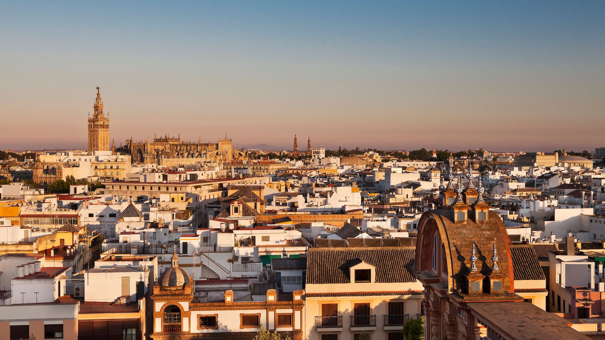 Seville cityscape at sunset with Giralda tower and cathedral, historic buildings.