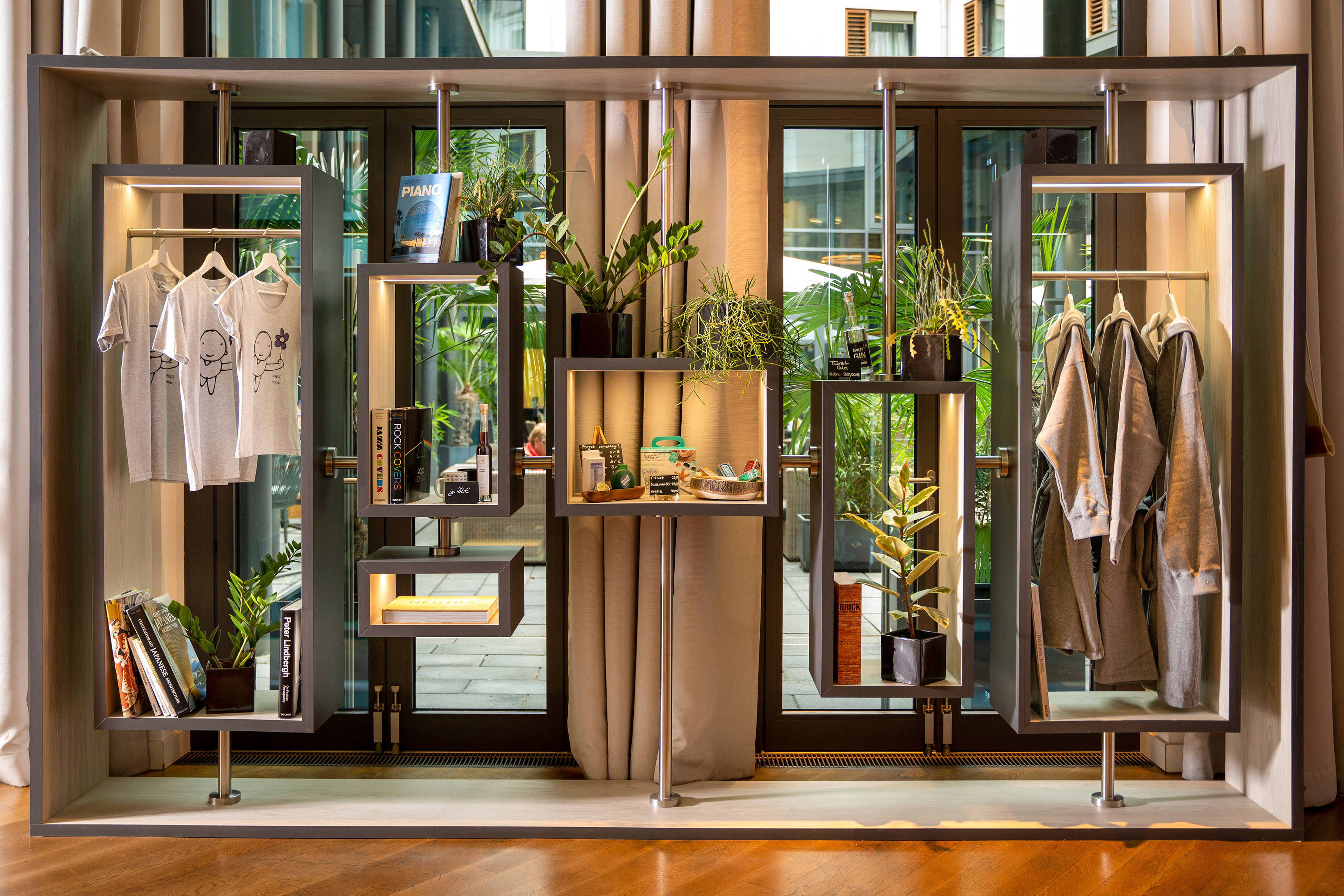 Modern retail display unit with t-shirts, robes, books, and plants, illuminated shelves.