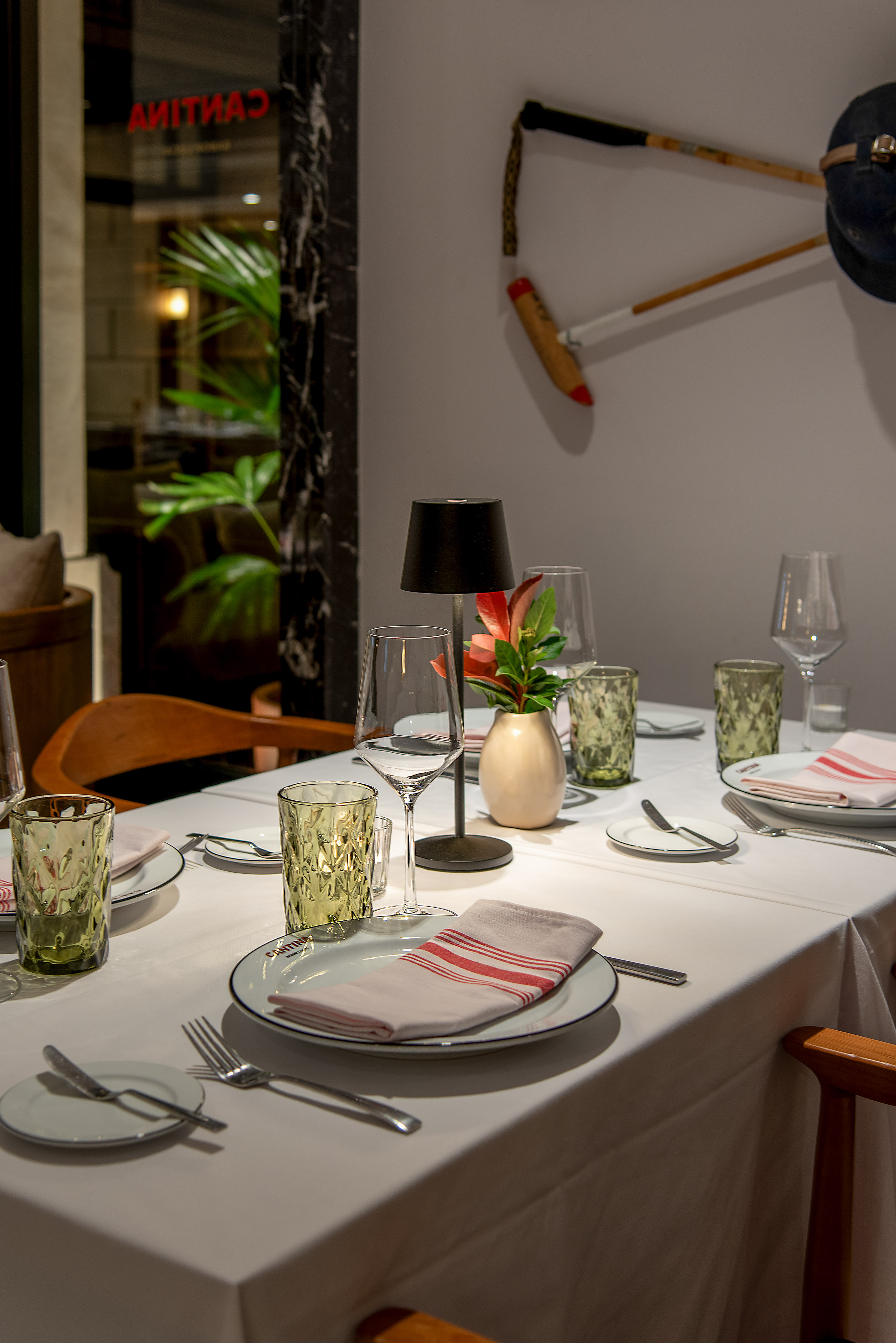 Restaurant table setting with plates, glasses, lamp, and flowers. Polo mallets on wall.