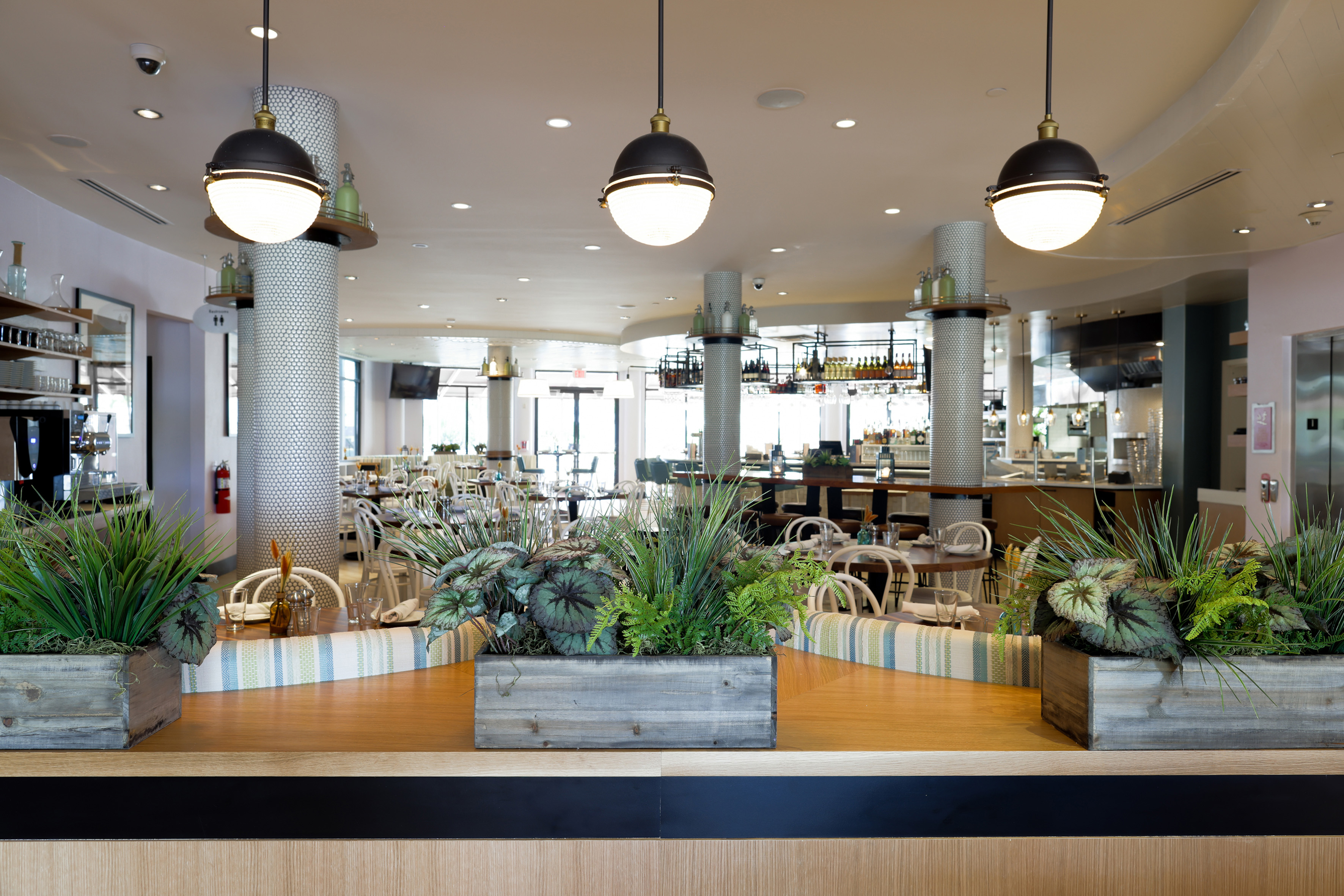 Modern restaurant interior with dining tables, bar area, and decorative planters.