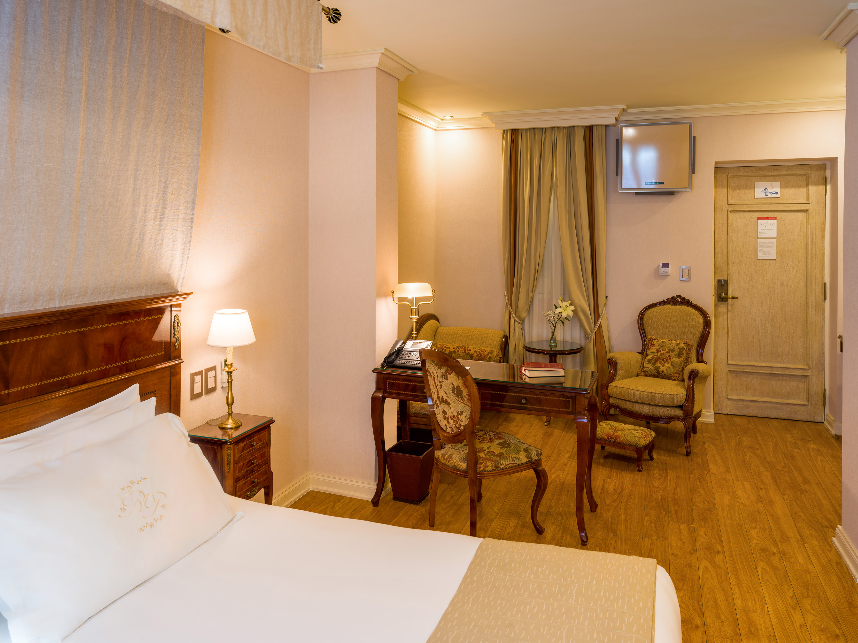 Elegant hotel bedroom with classic wooden furniture, bed, desk, and armchair.