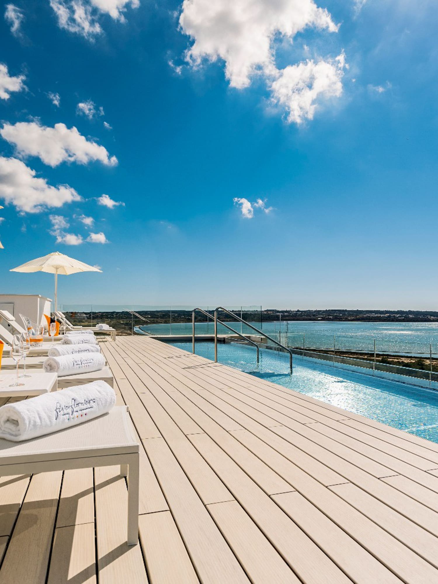 a deck with chairs and umbrellas and a pool with water in the background