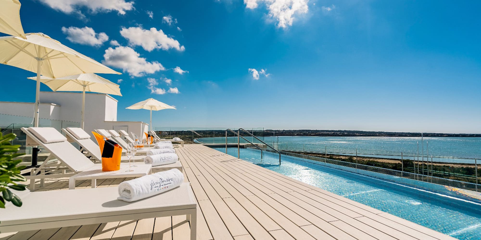 a deck with chairs and umbrellas and a pool with water in the background