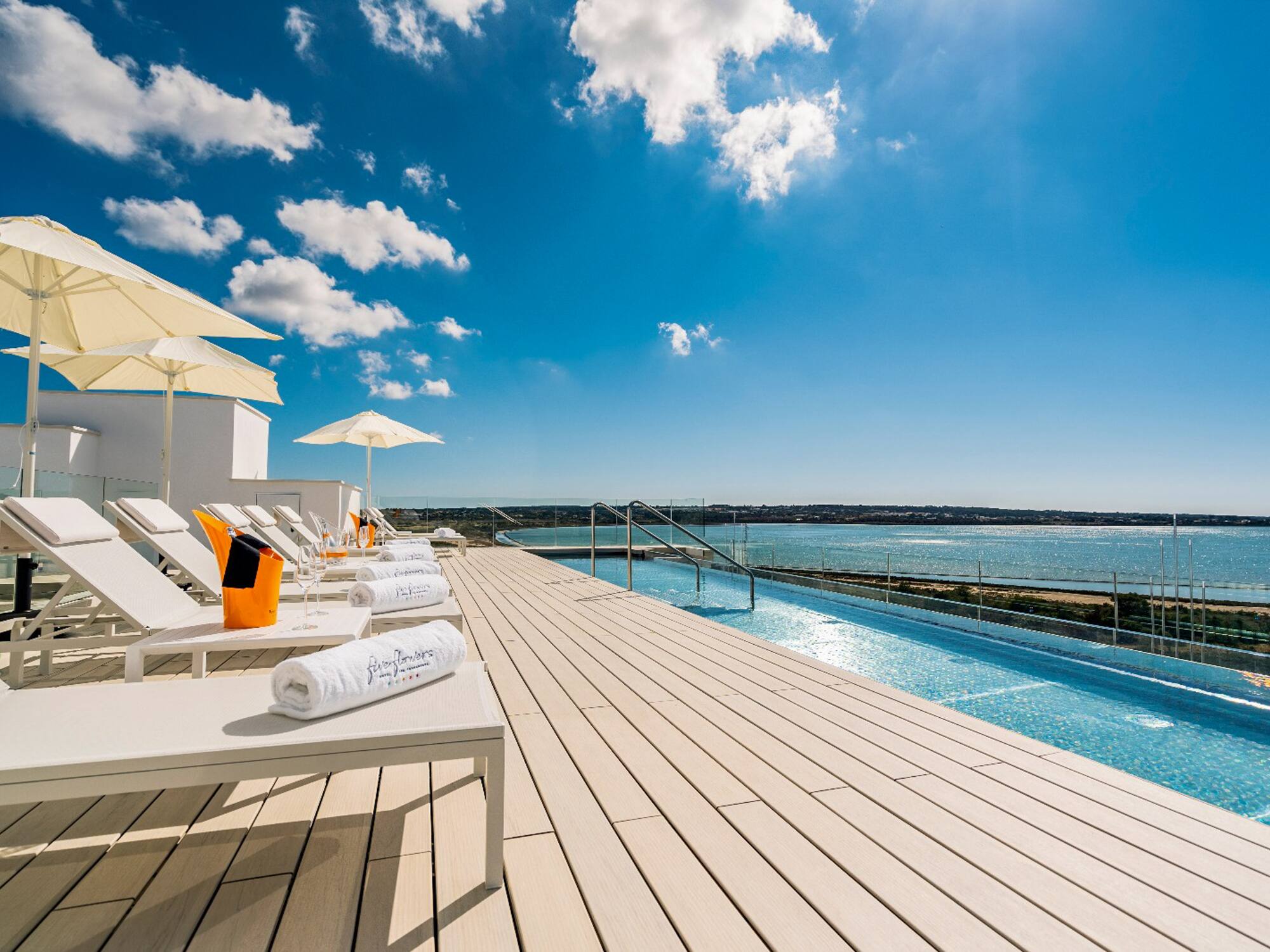 a deck with chairs and umbrellas and a pool with water in the background