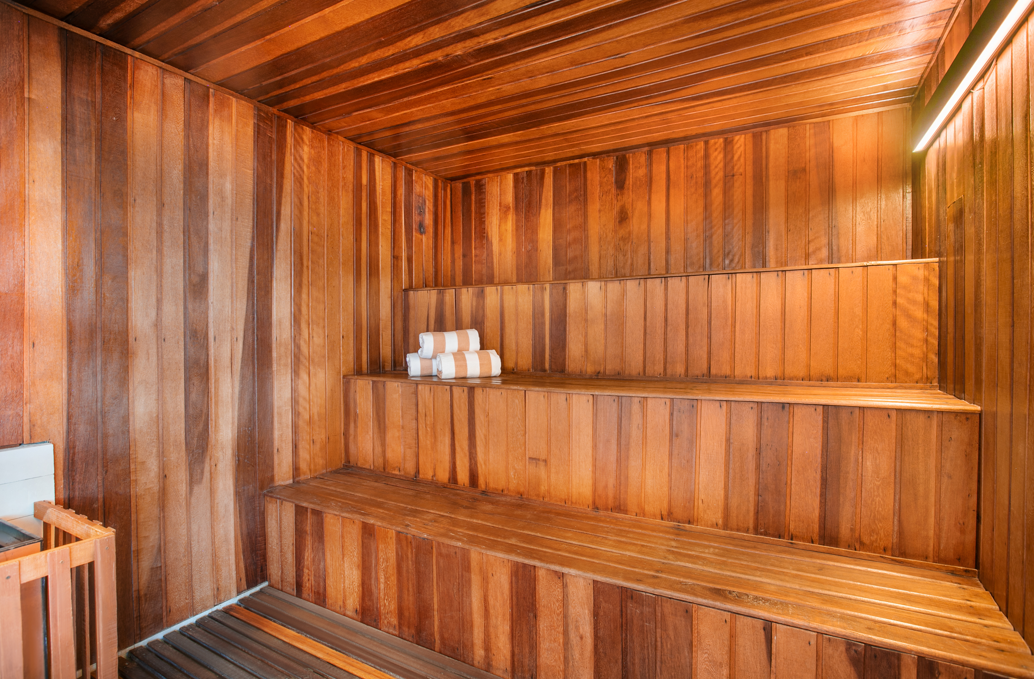 Bright wooden sauna with multi-tiered benches, towels, and heater.