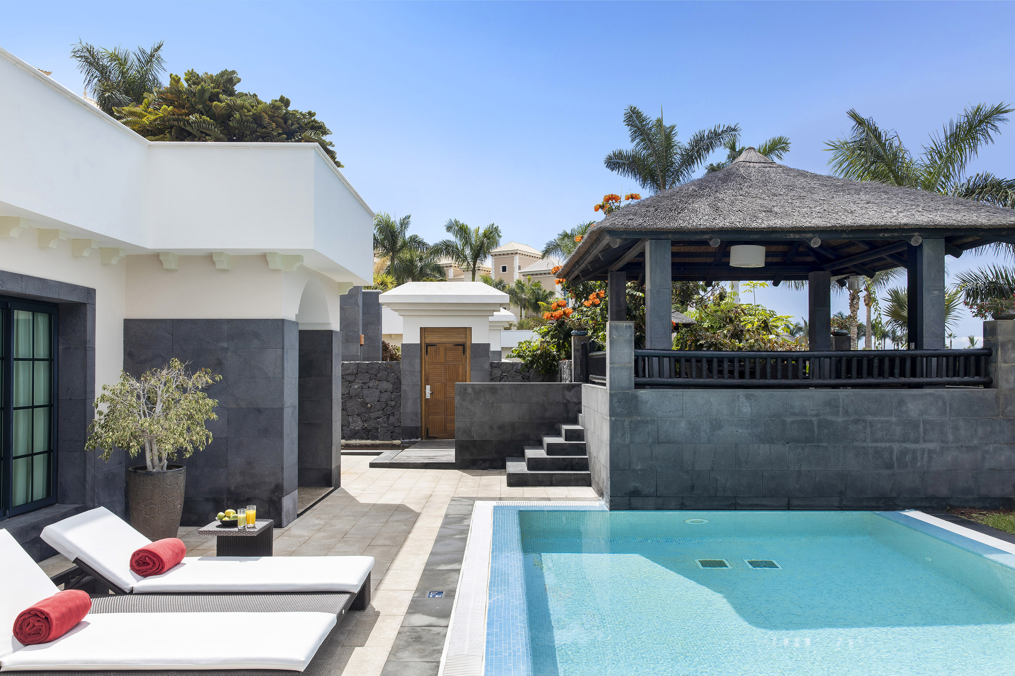 Resort private pool with loungers, tropical garden, and thatched gazebo.