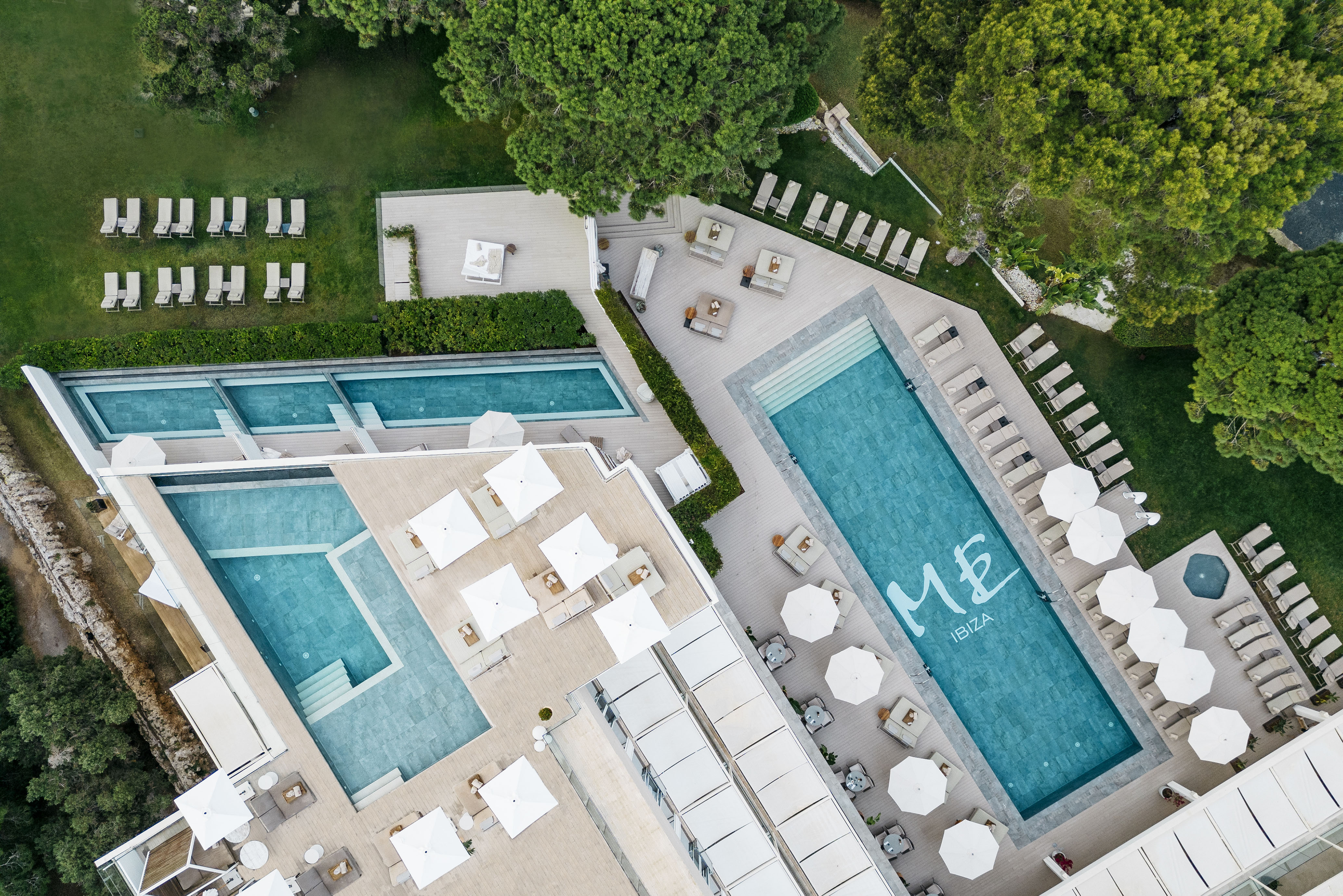 ME Ibiza hotel aerial view: multiple pools, sun loungers, green gardens.