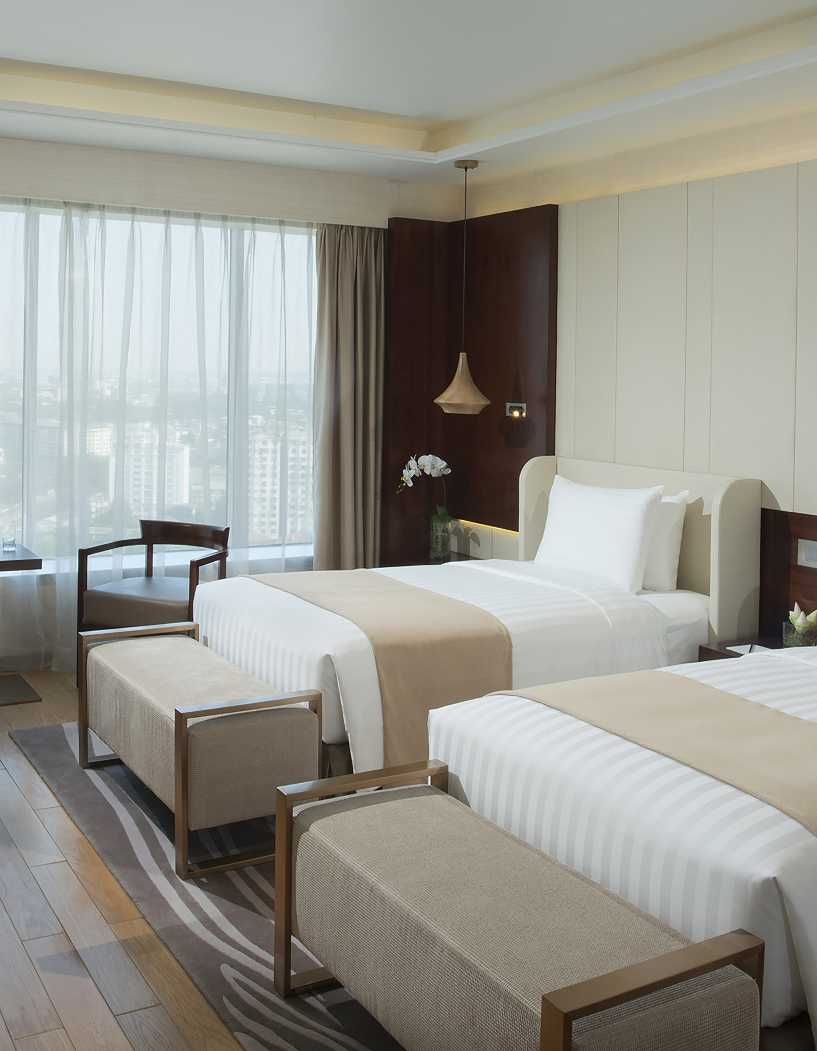 Modern hotel room with two twin beds, city view, and elegant decor.