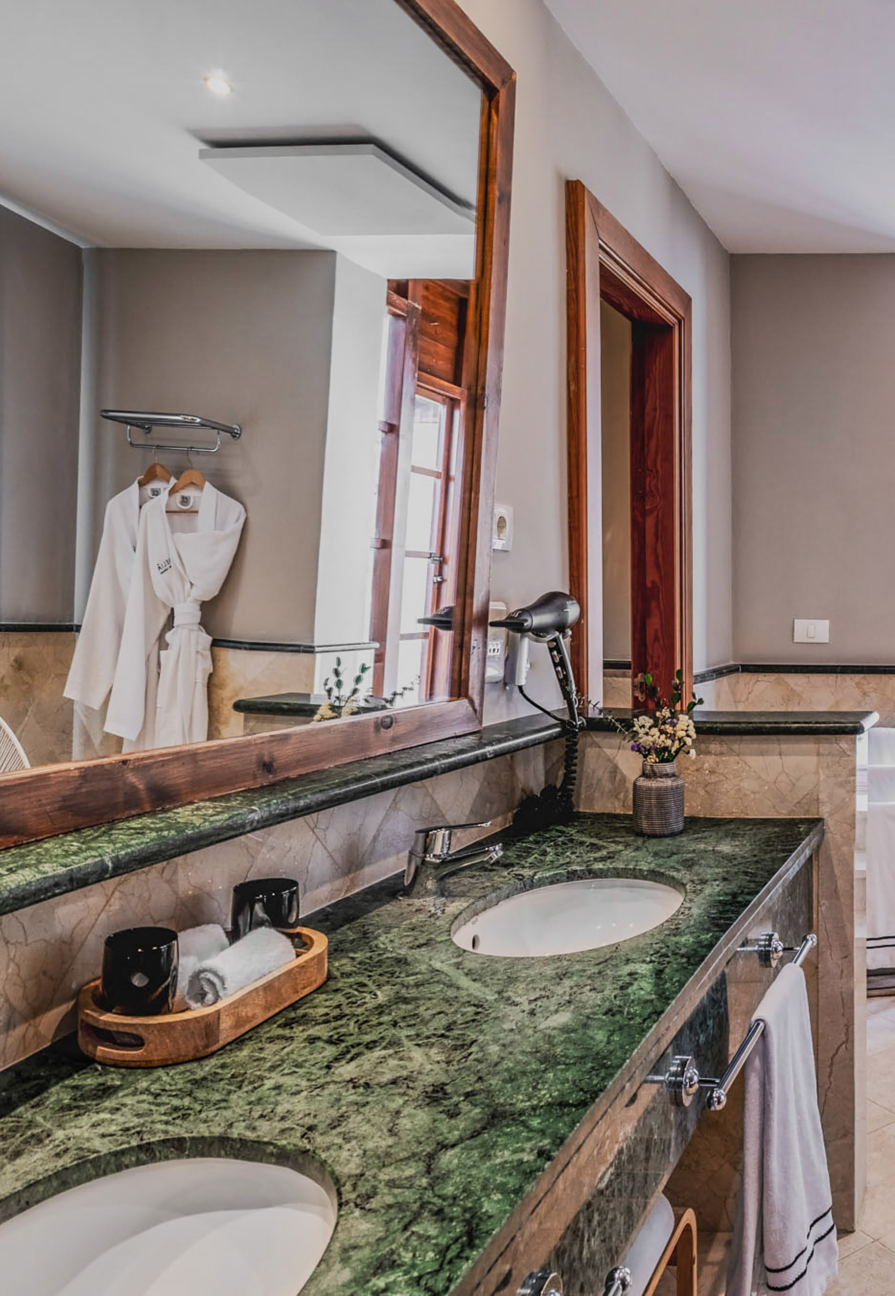 Luxury bathroom with green marble double vanity, two sinks, mirror, and bathrobes.