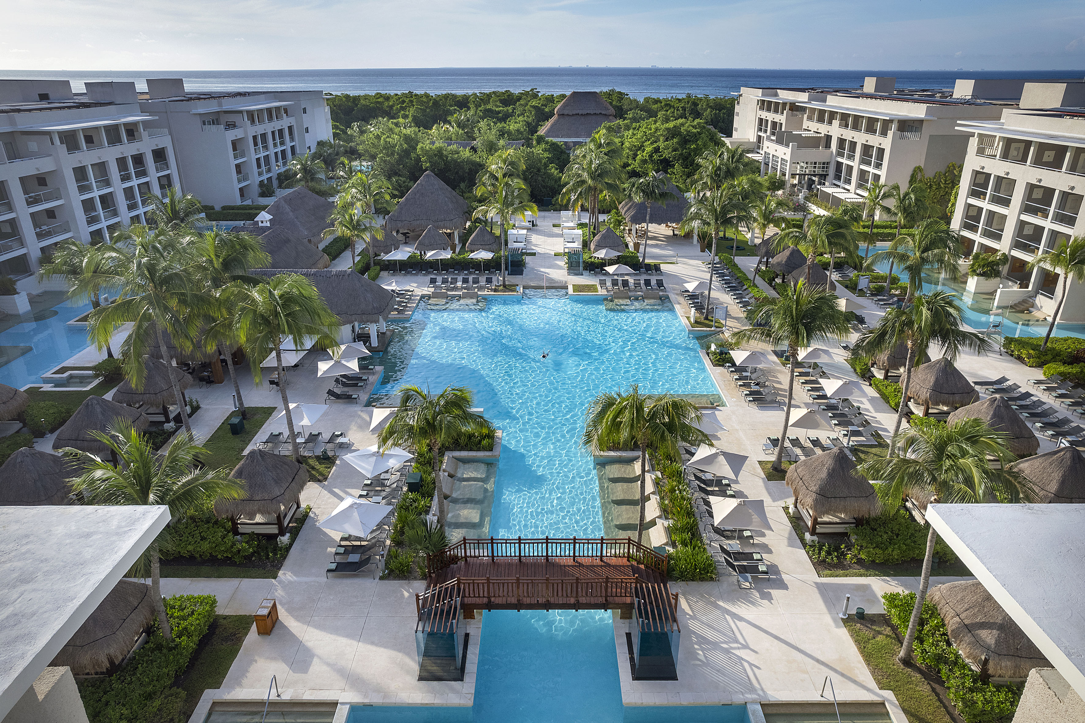 Aerial view of luxury hotel resort, large pool, palm trees, cabanas, ocean.