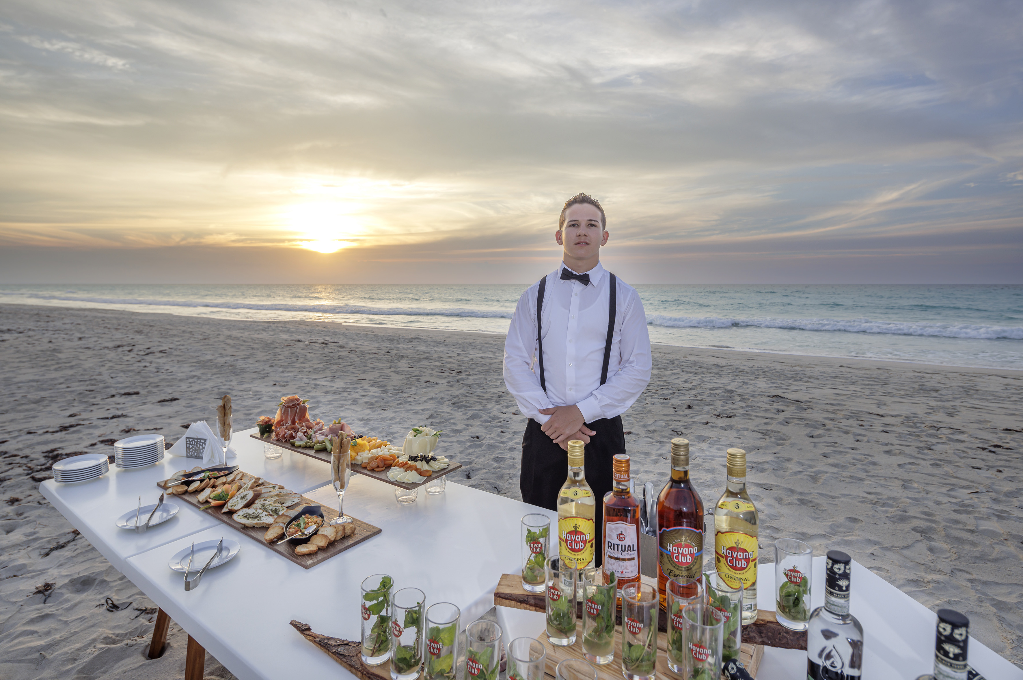 a man standing in front of a table with drinks and food on the beach