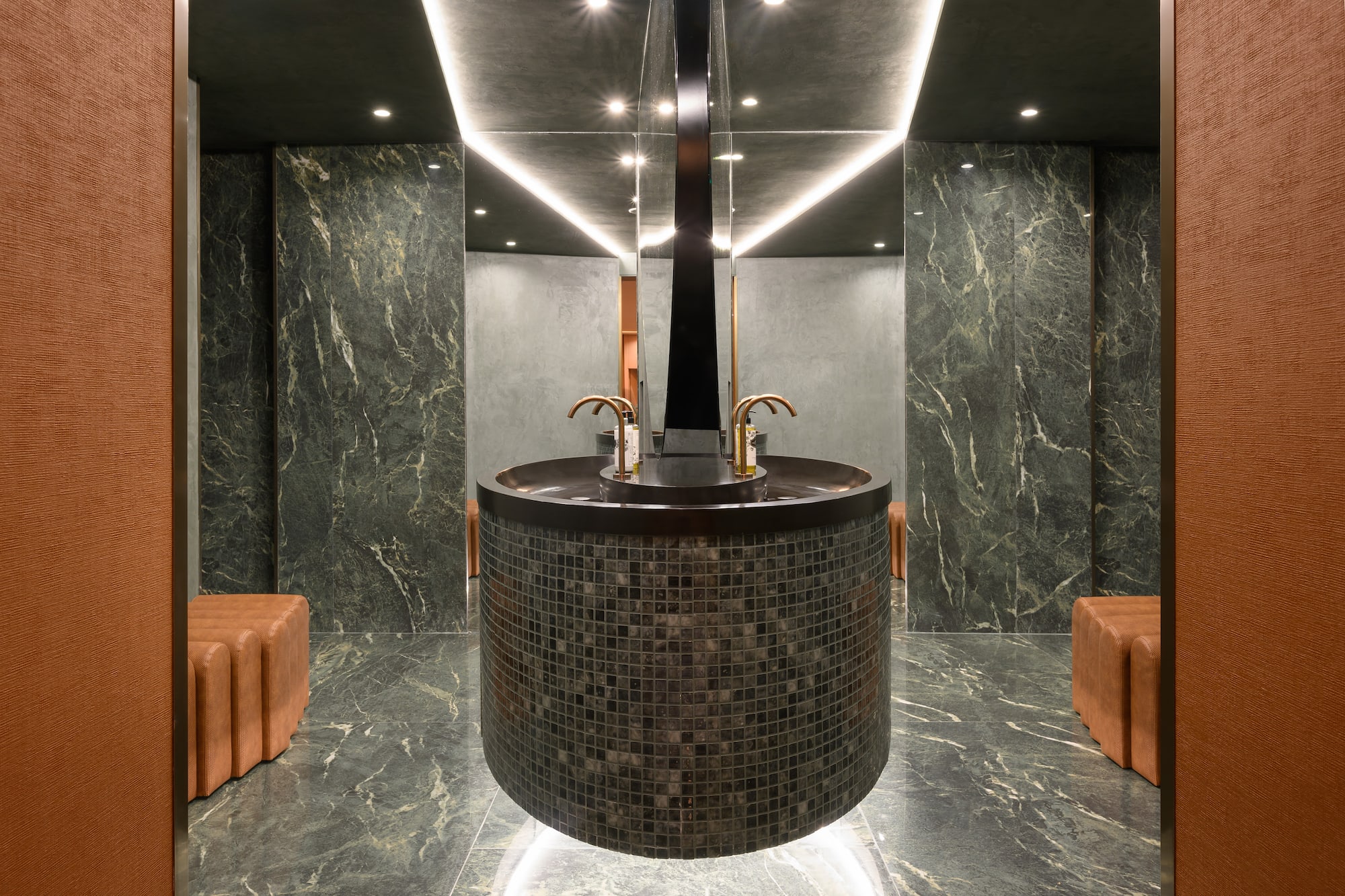 Luxurious green marble bathroom, circular tiled vanity, gold faucets.