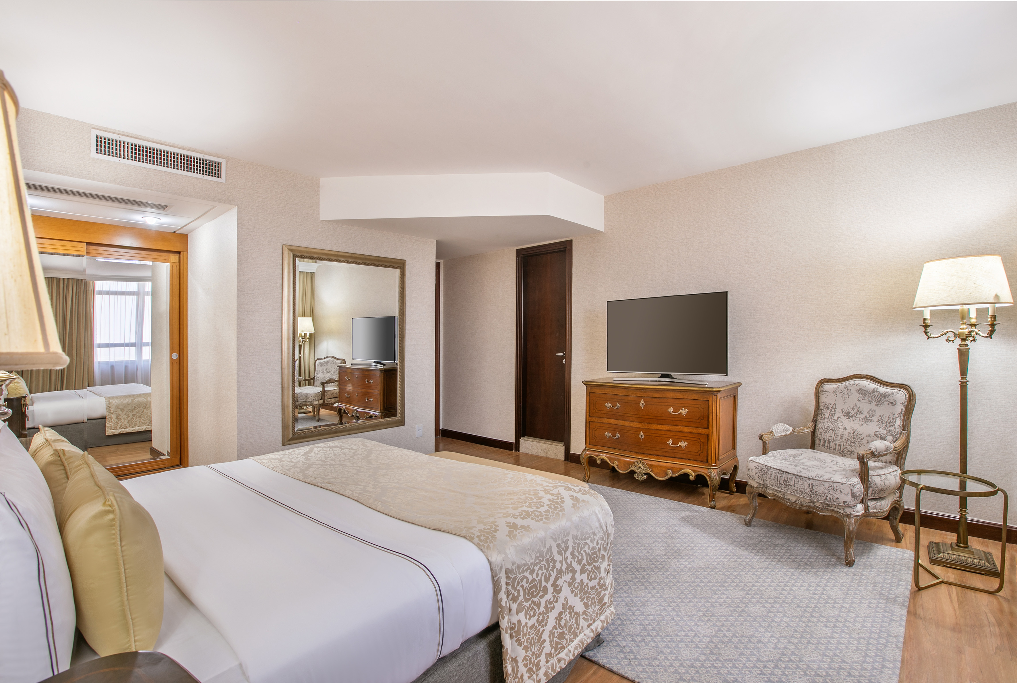 Luxury hotel room with bed, TV dresser, classic armchair, and mirror.