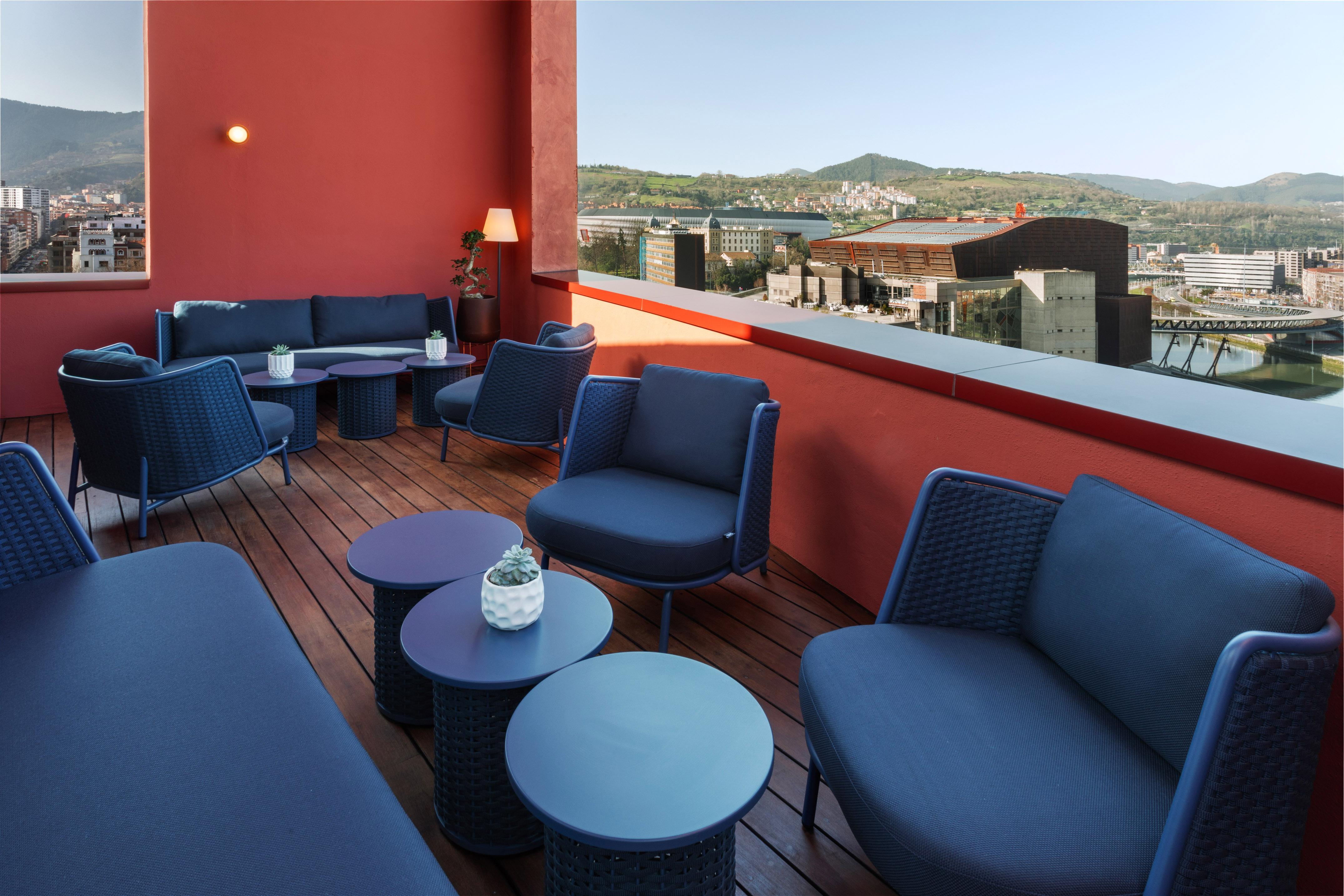 Modern outdoor lounge with blue furniture, red walls, and city skyline view.