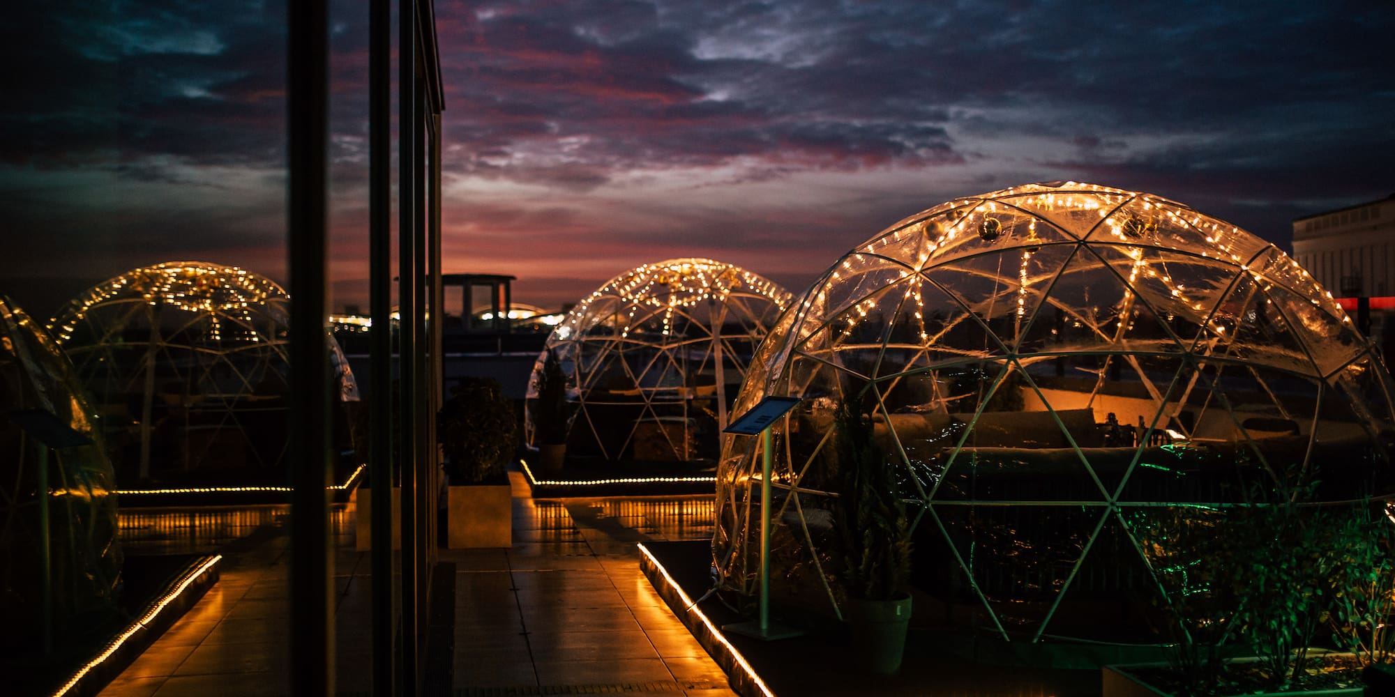 Outdoor rooftop dining igloos glowing with string lights at sunset.