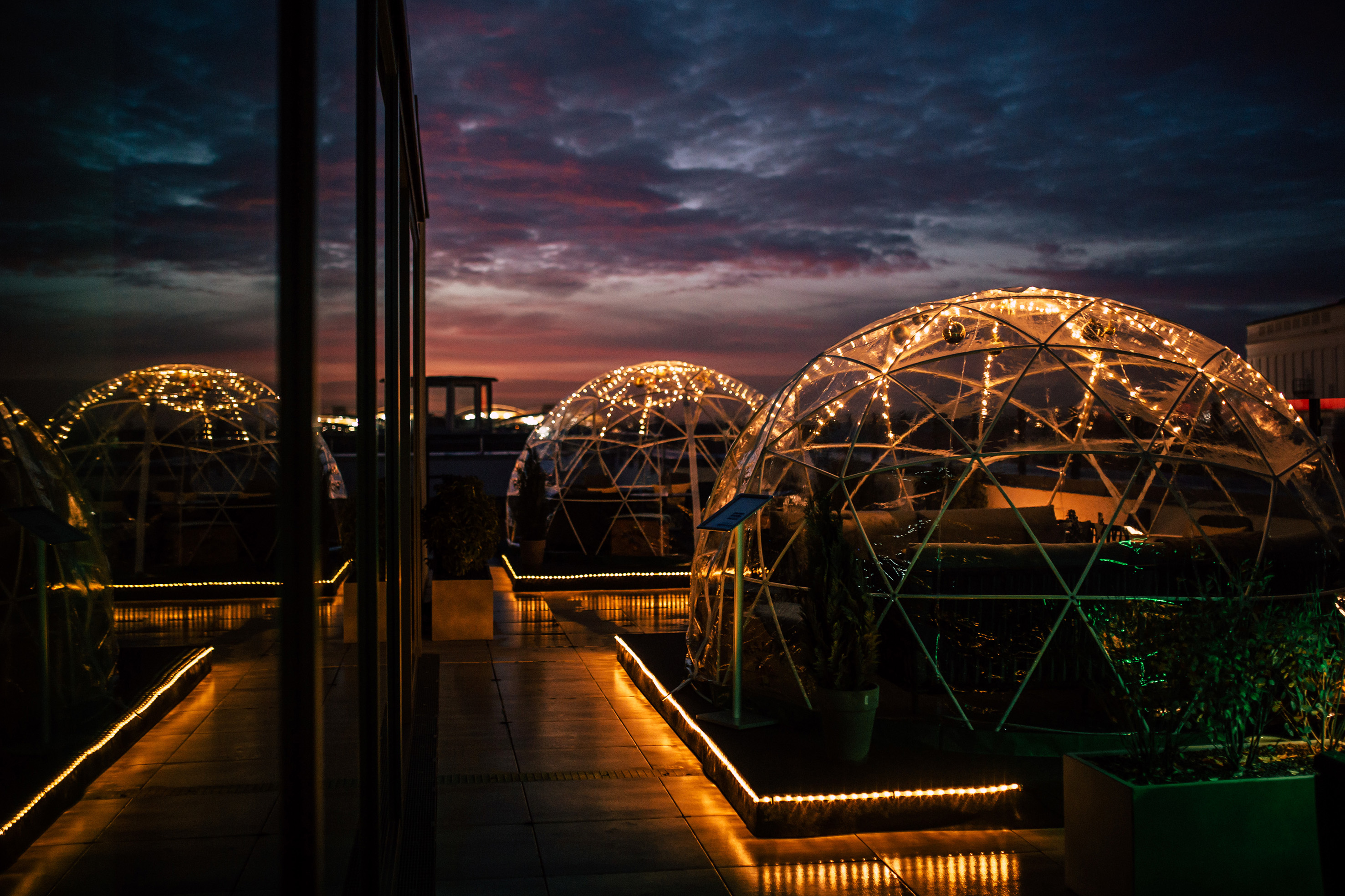 Outdoor rooftop dining igloos glowing with string lights at sunset.
