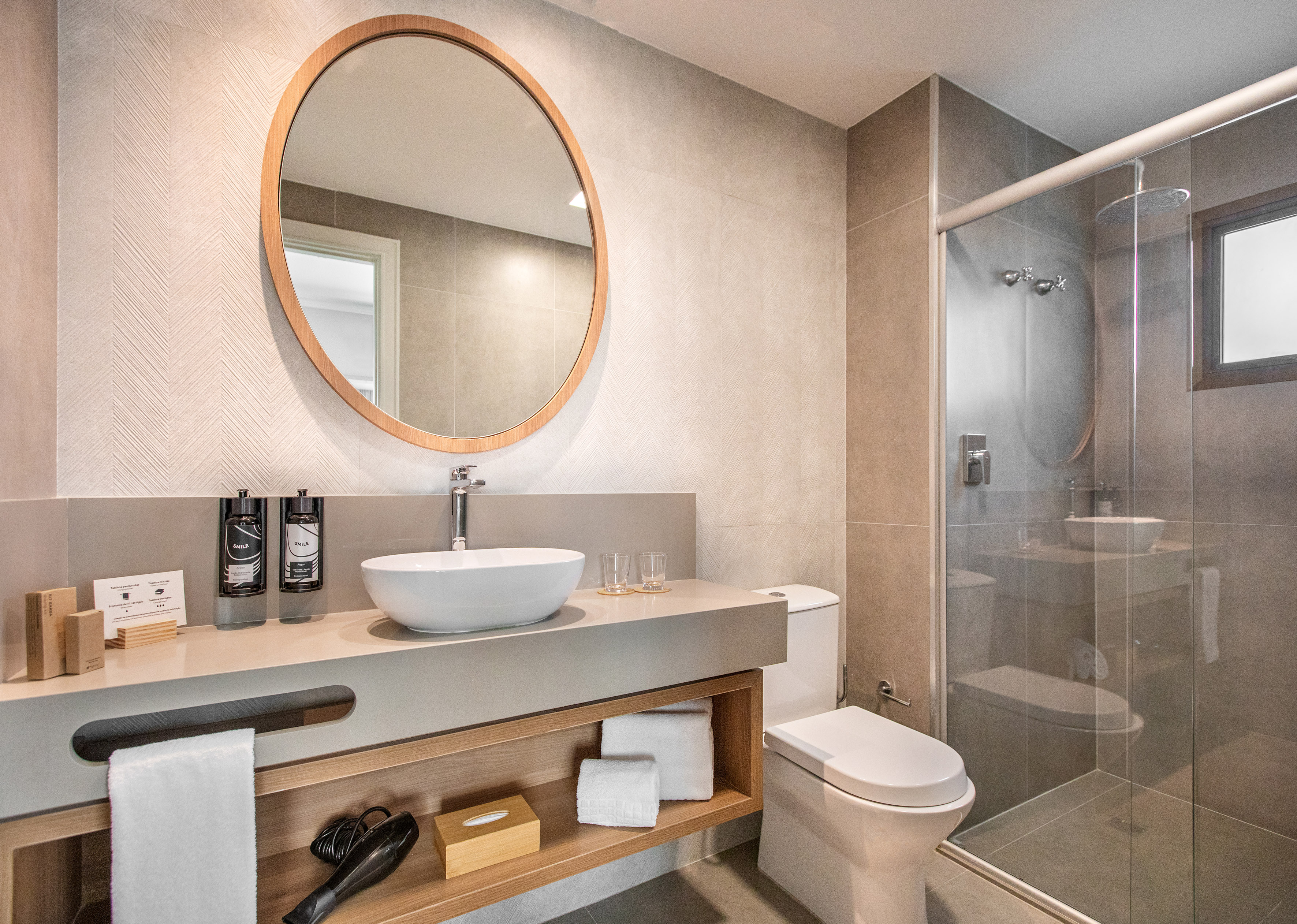 Modern bathroom with round mirror, vessel sink, floating vanity, and glass shower.