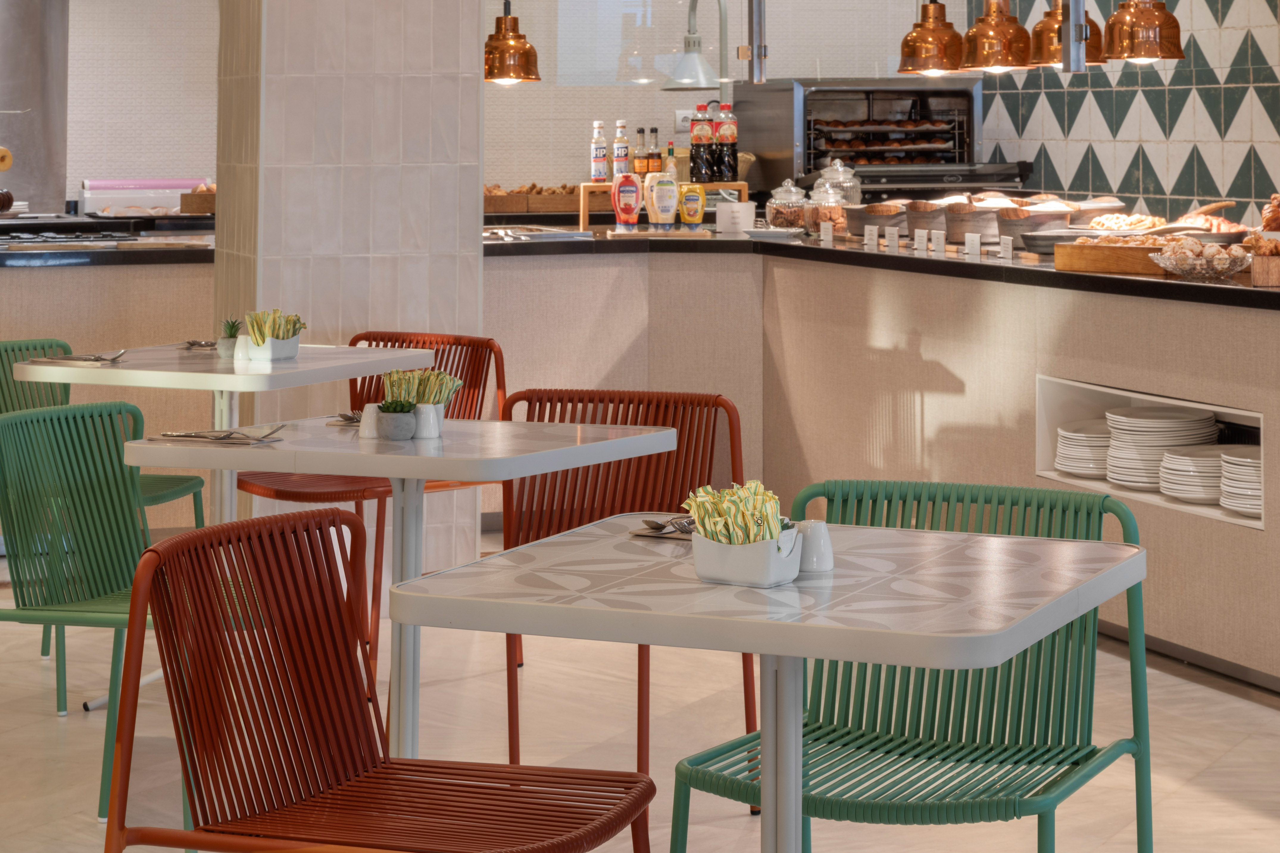 Modern cafe interior with breakfast buffet and colorful dining chairs.