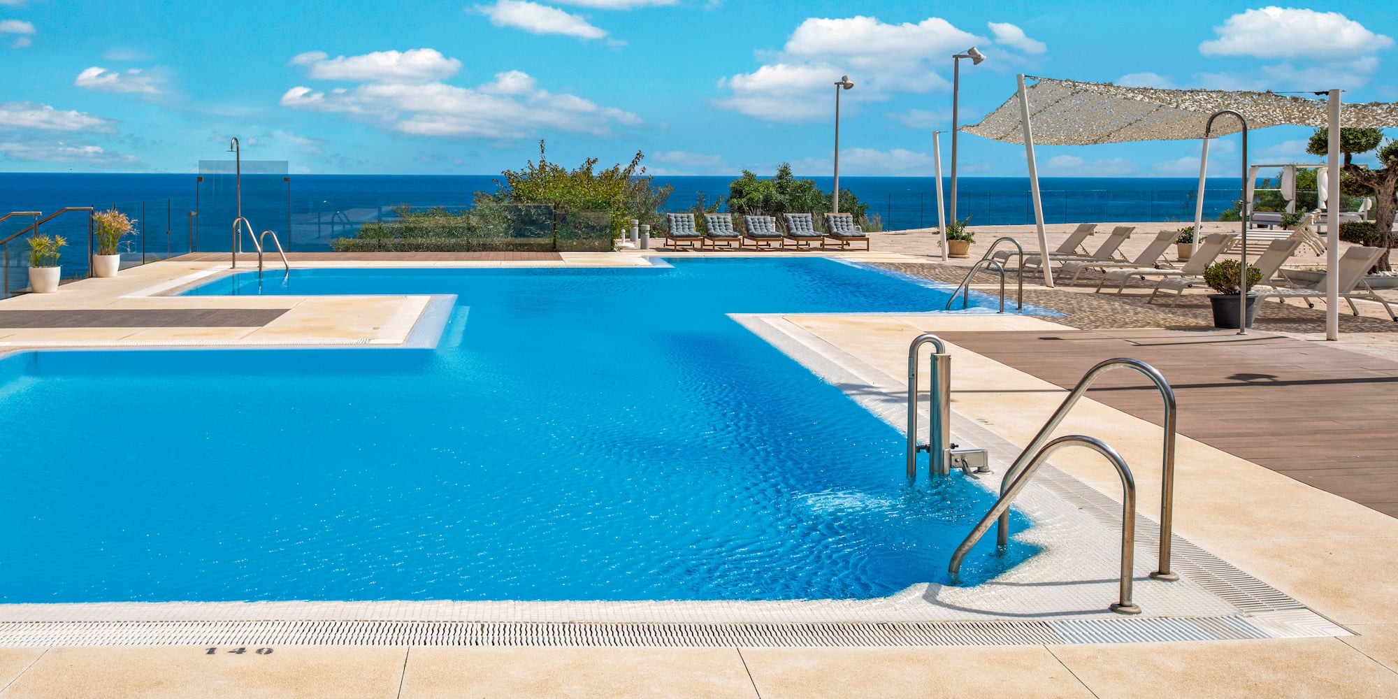 Sunny resort pool with ocean view and sun loungers.