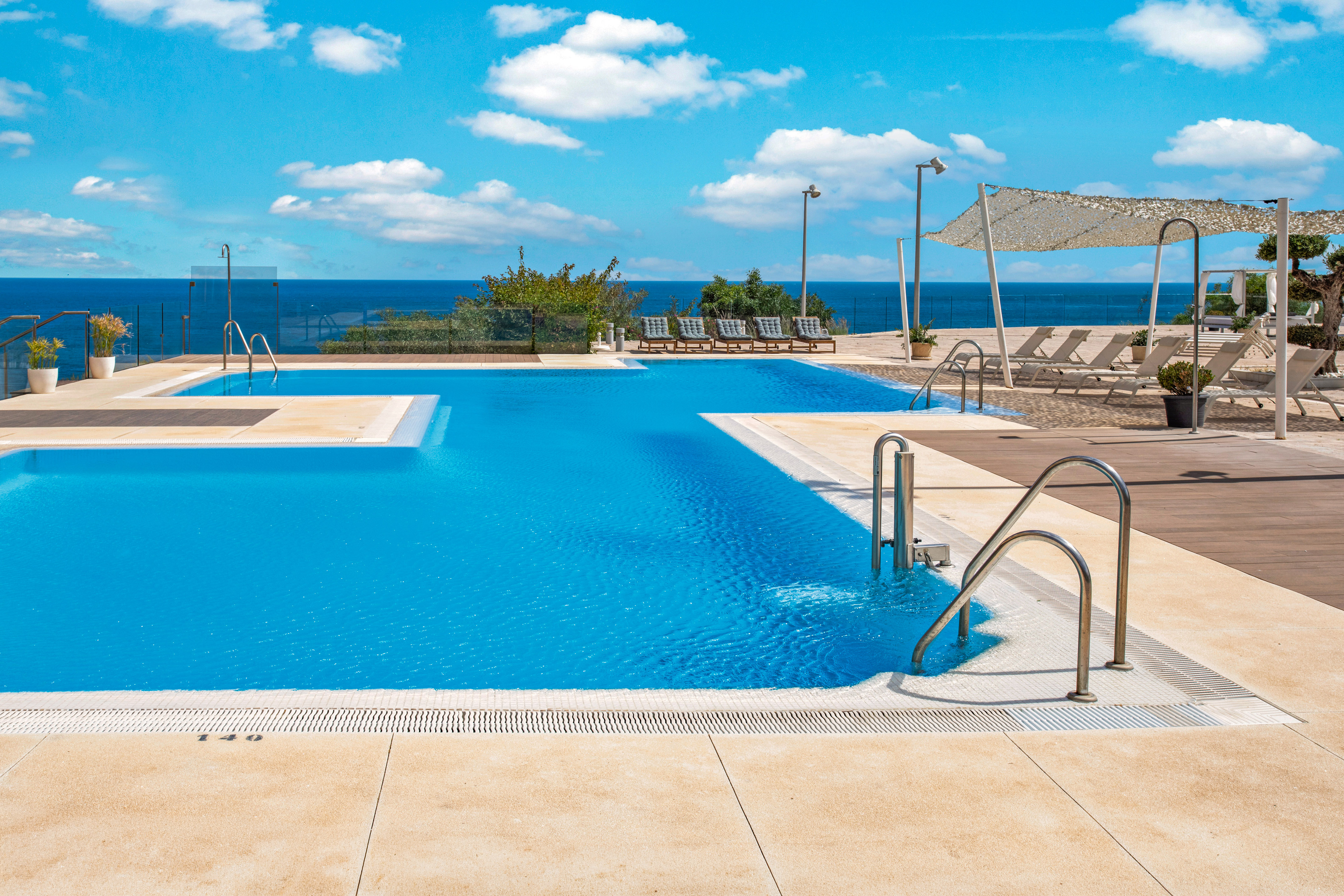 Sunny resort pool with ocean view and sun loungers.