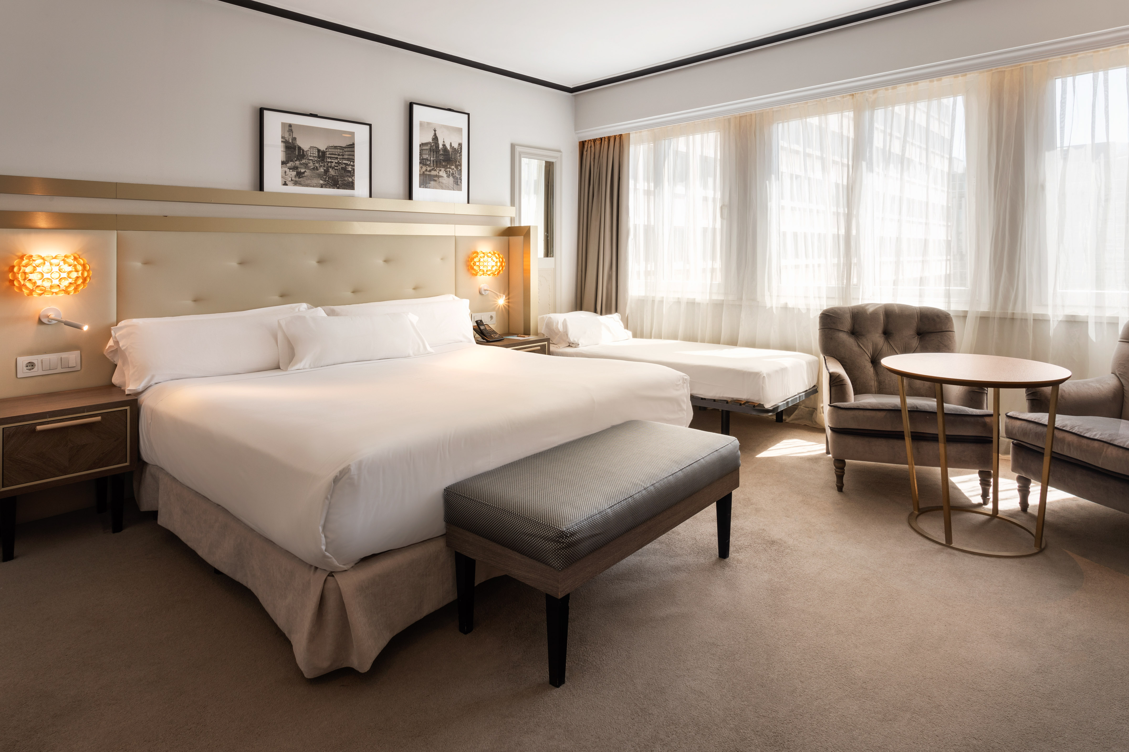 Modern hotel room with king bed, seating area, and bright windows.
