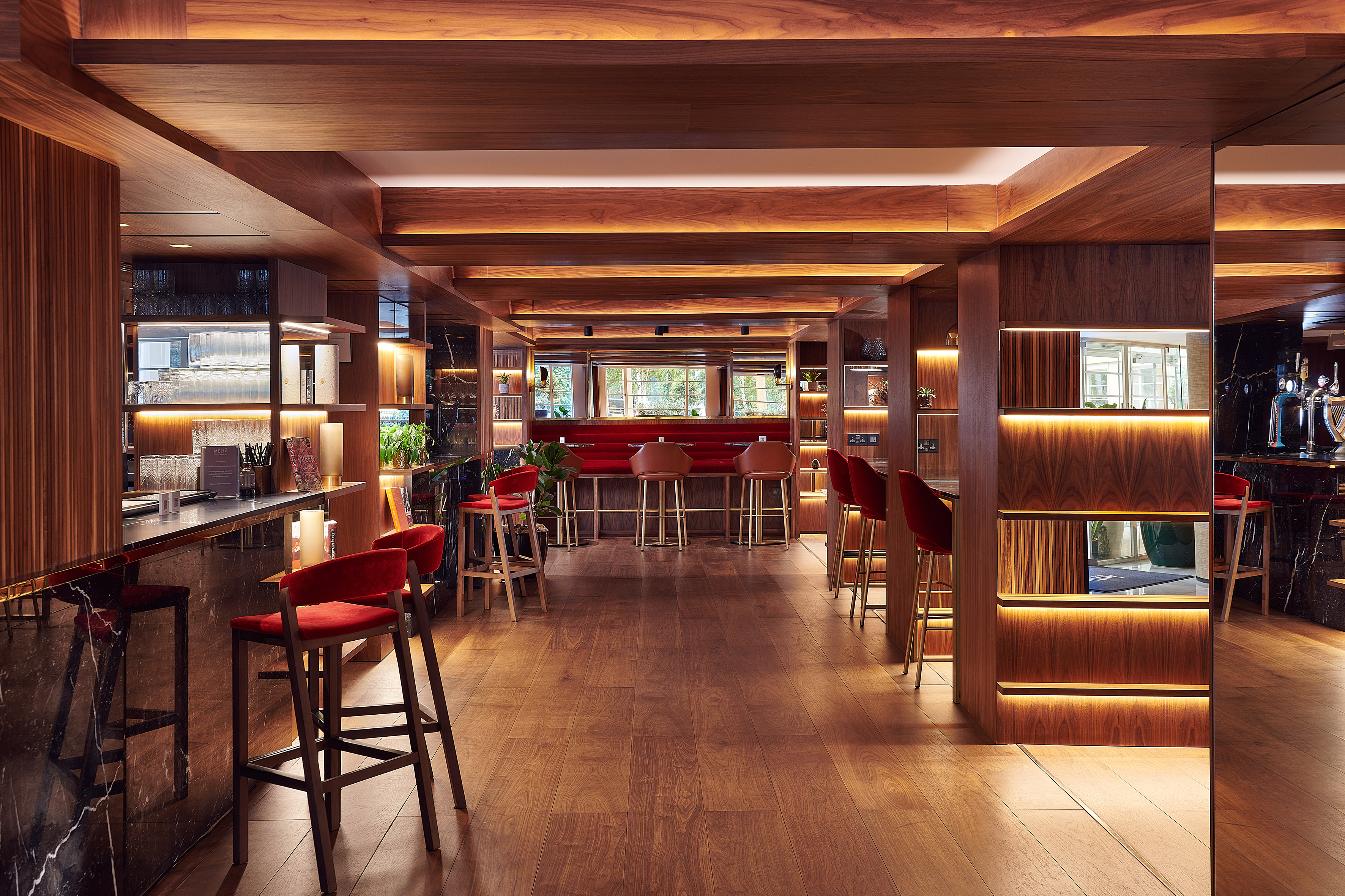 Upscale bar lounge with warm wood, ambient lighting, and red velvet bar stools.