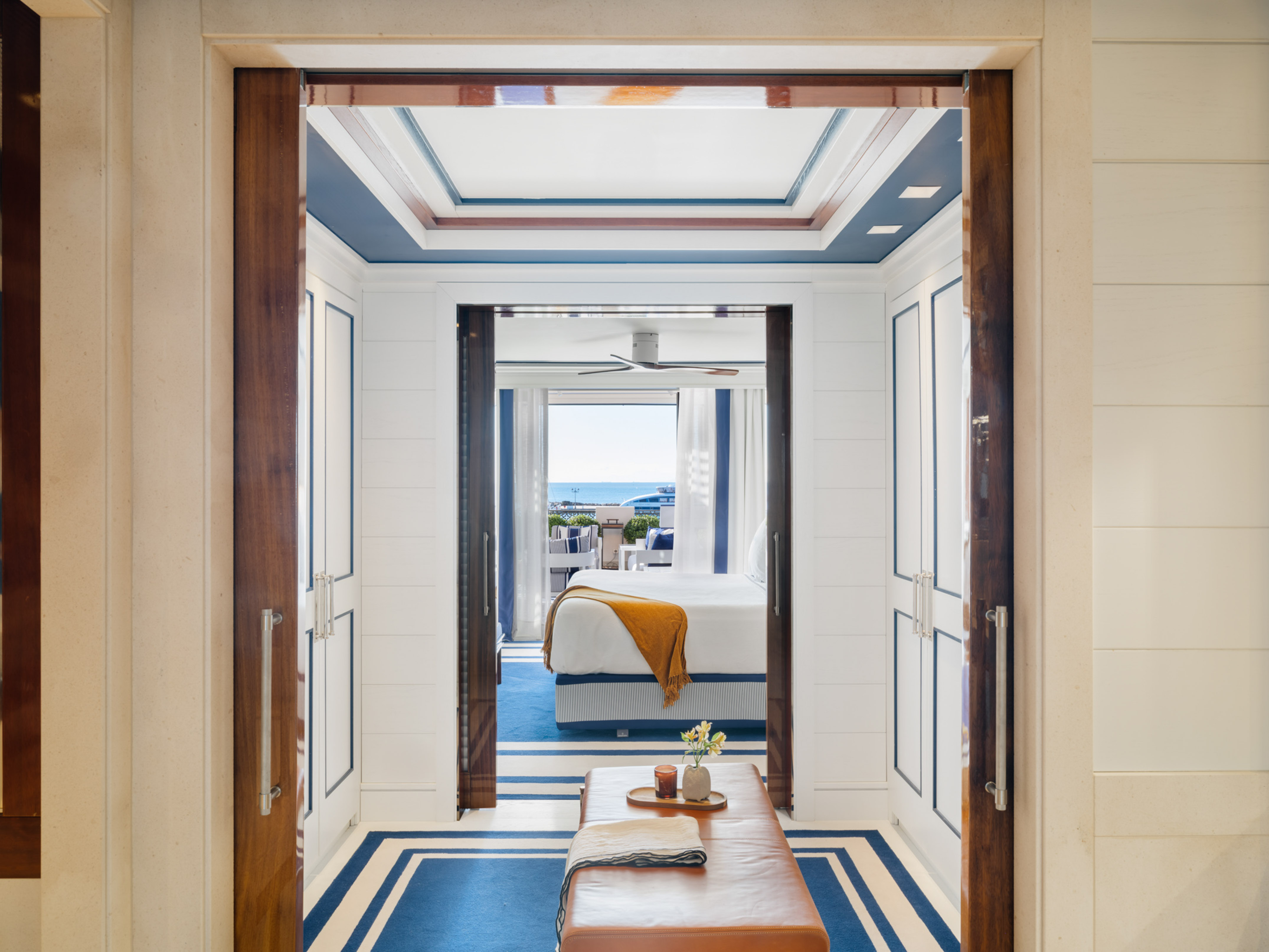 Luxury bedroom with ocean view, blue nautical decor, and sliding wood doors.