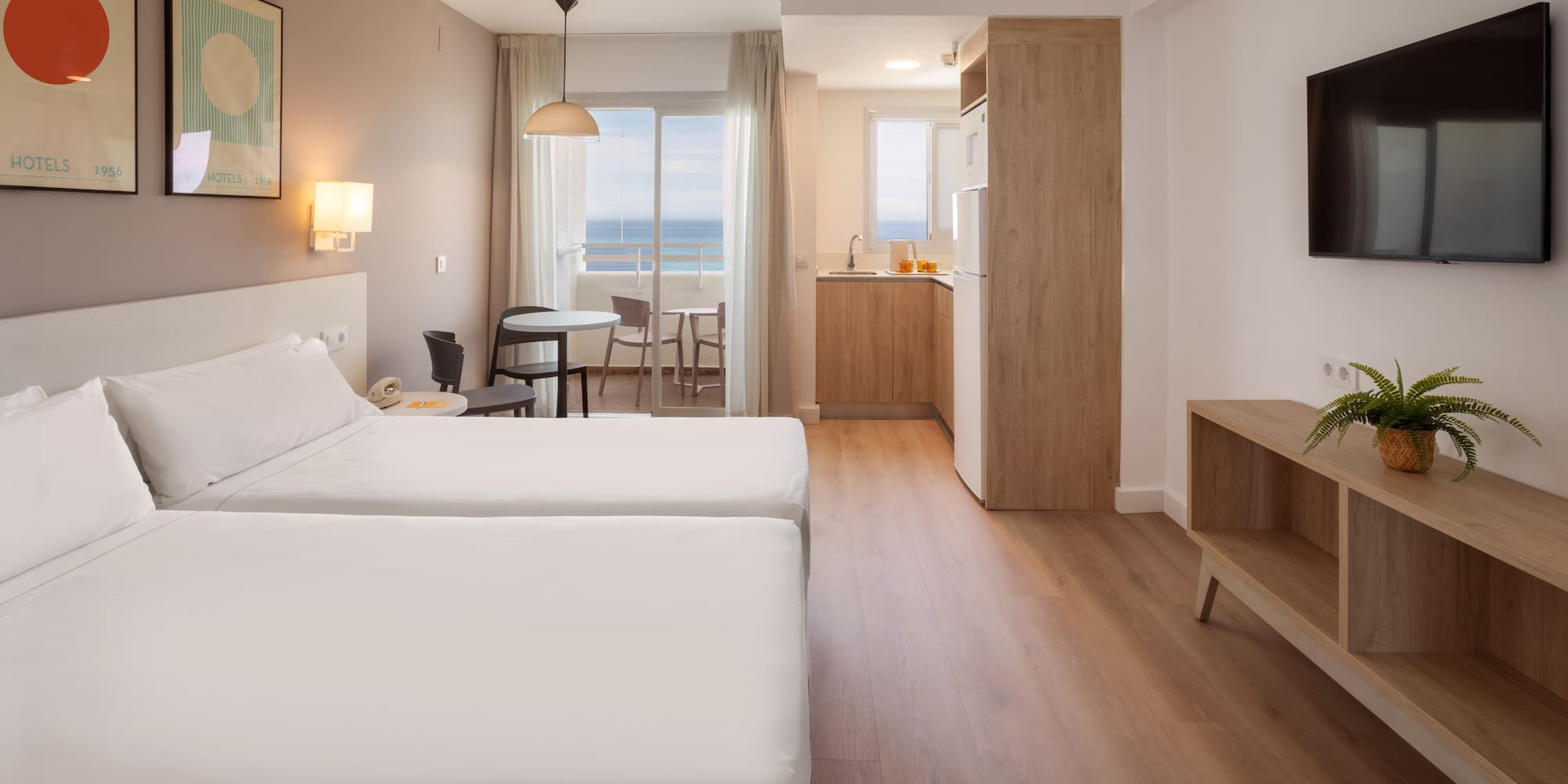 Modern hotel room with twin beds, kitchenette, and ocean view balcony.