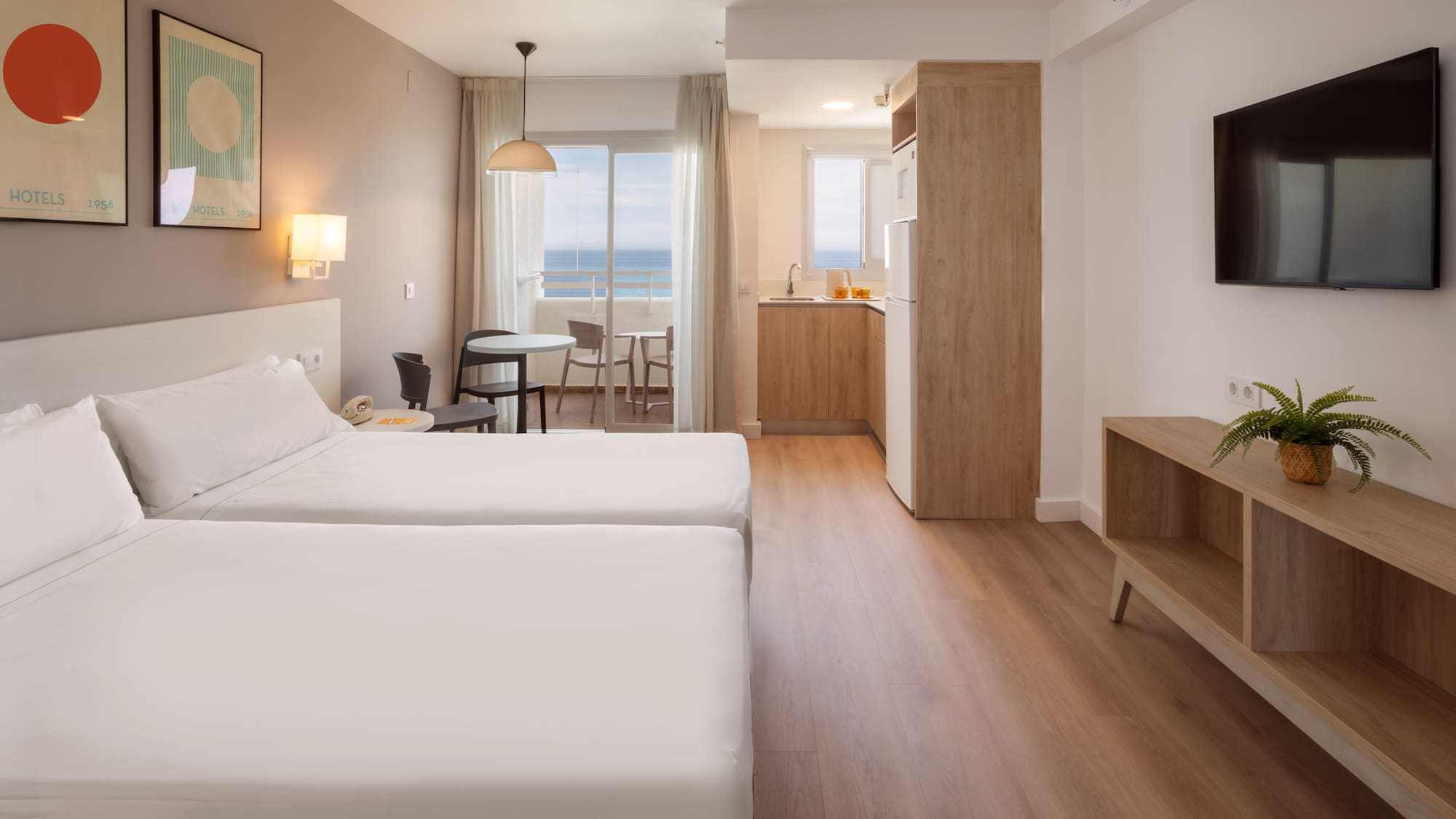 Modern hotel studio apartment with twin beds, kitchenette, balcony, and sea view.